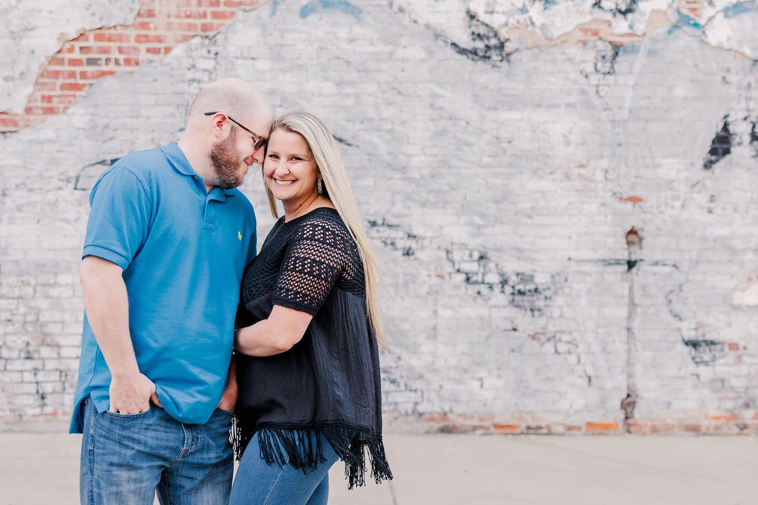 A couple shares an intimate moment against a rustic brick wall background.