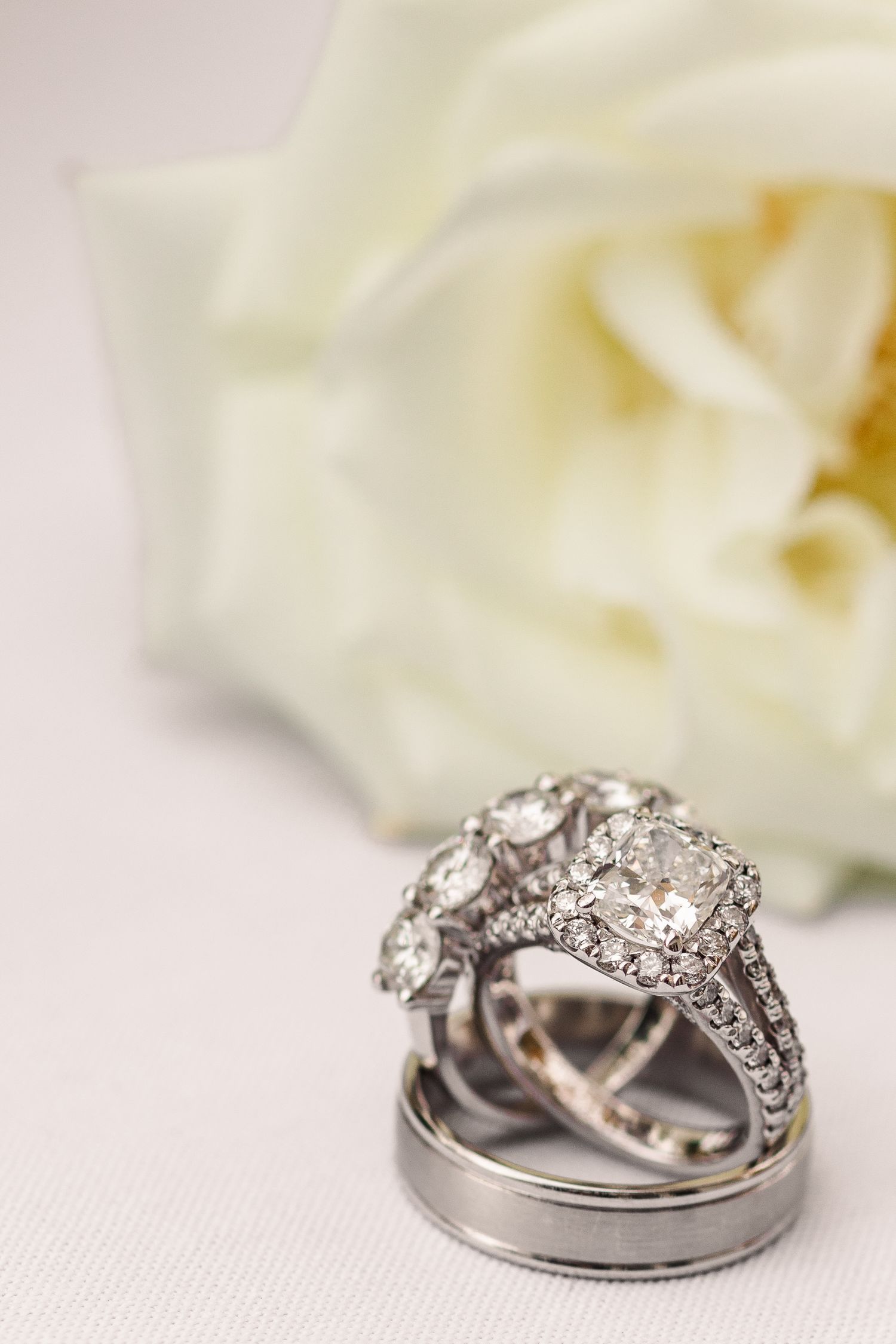 Diamond engagement ring and wedding band set with white rose backdrop.