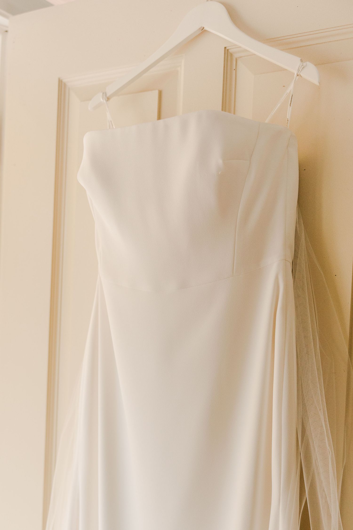 Elegant white wedding dress hanging on display against a cream colored door.