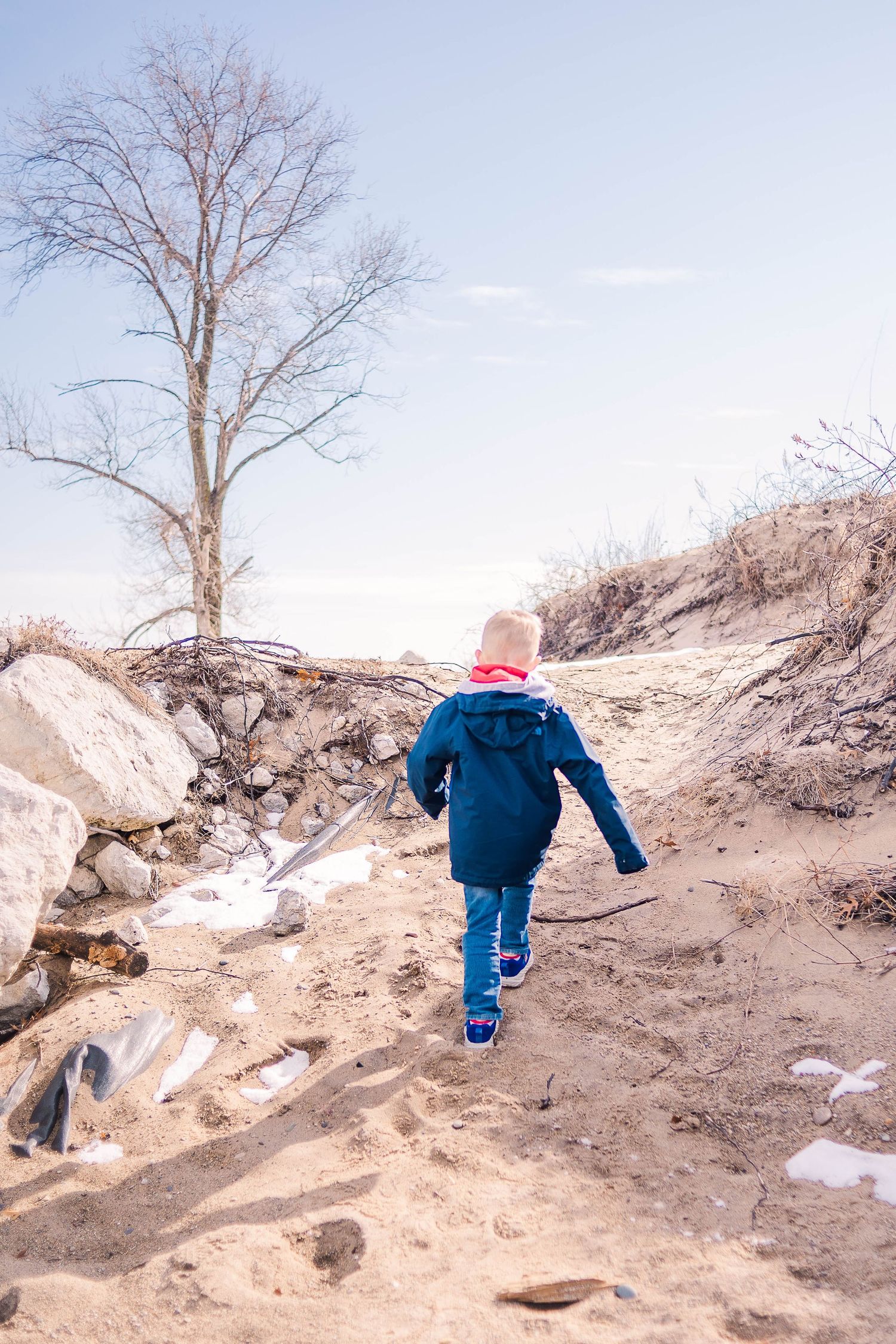 Someone climbing a sandy hill path wearing a blue jacket on a winter day.
