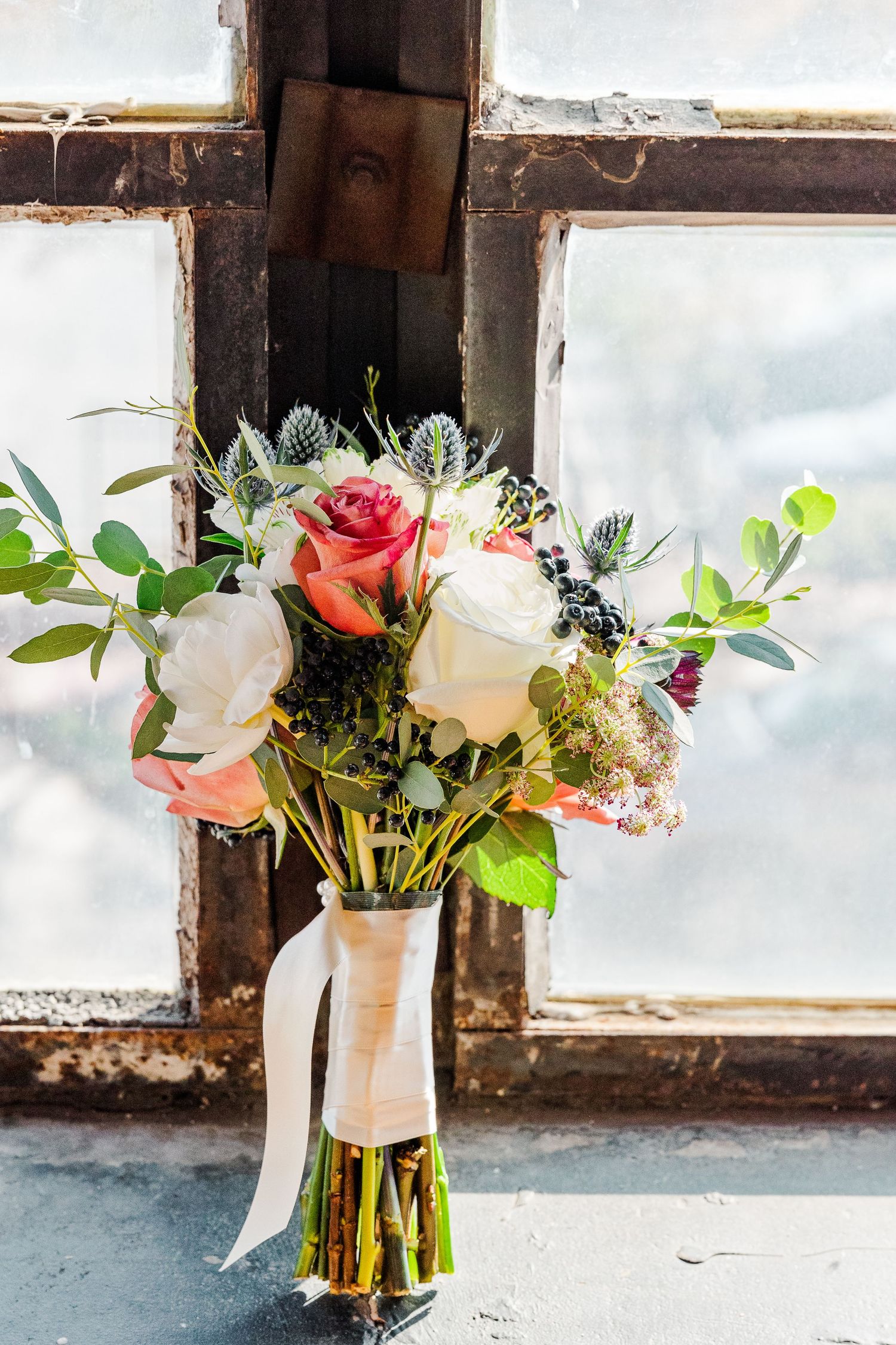 Bridal bouquet with white and pink roses tied with ribbon sitting on rustic windowsill.