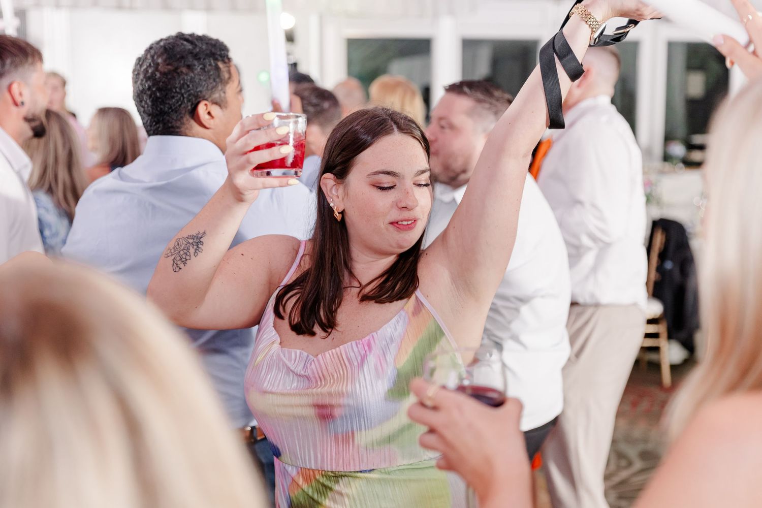Wedding guest takes a selfie while dancing and holding a drink at a lively wedding reception.