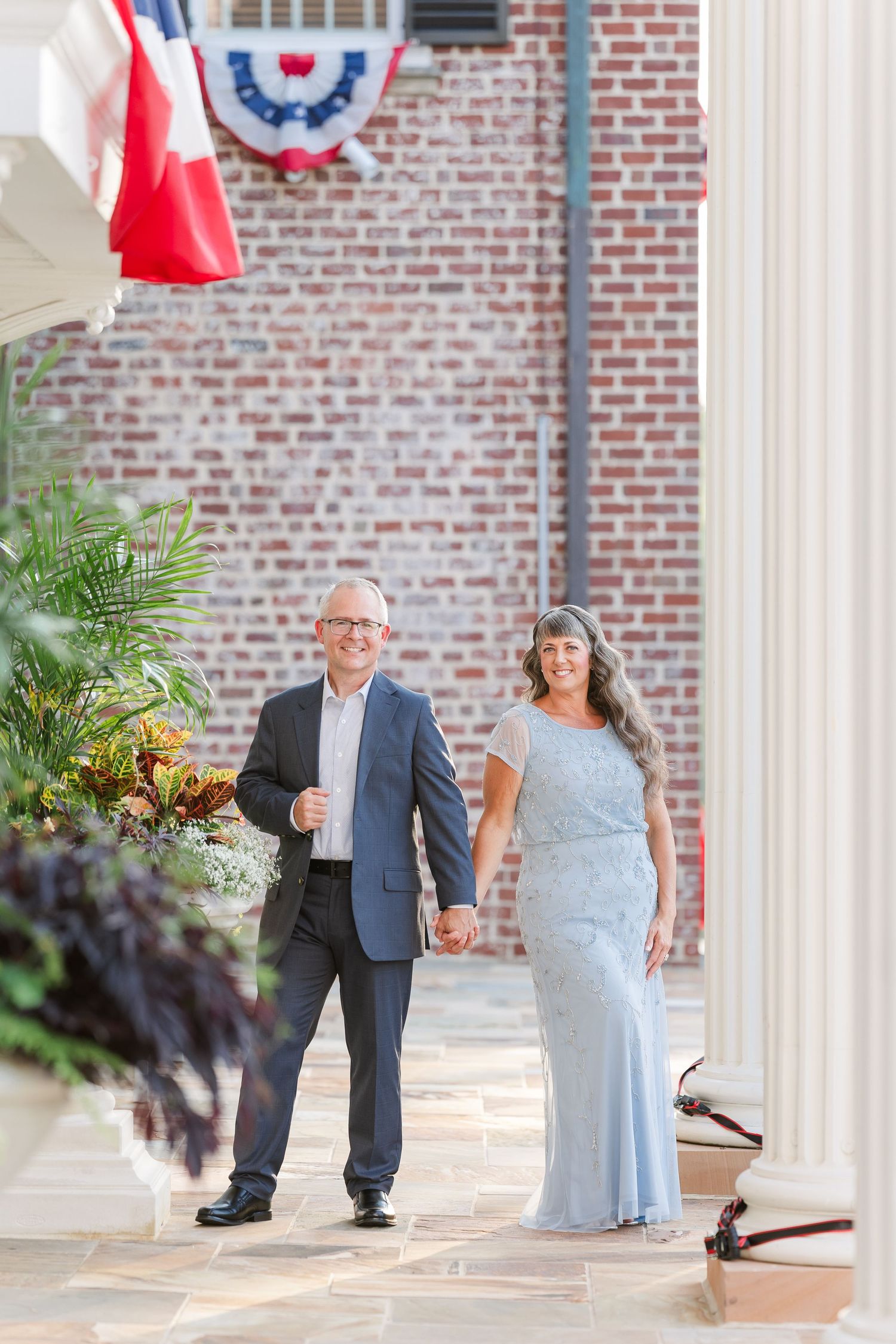 Couple holding hands smiling in front of brick building with patriotic bunting decorations.