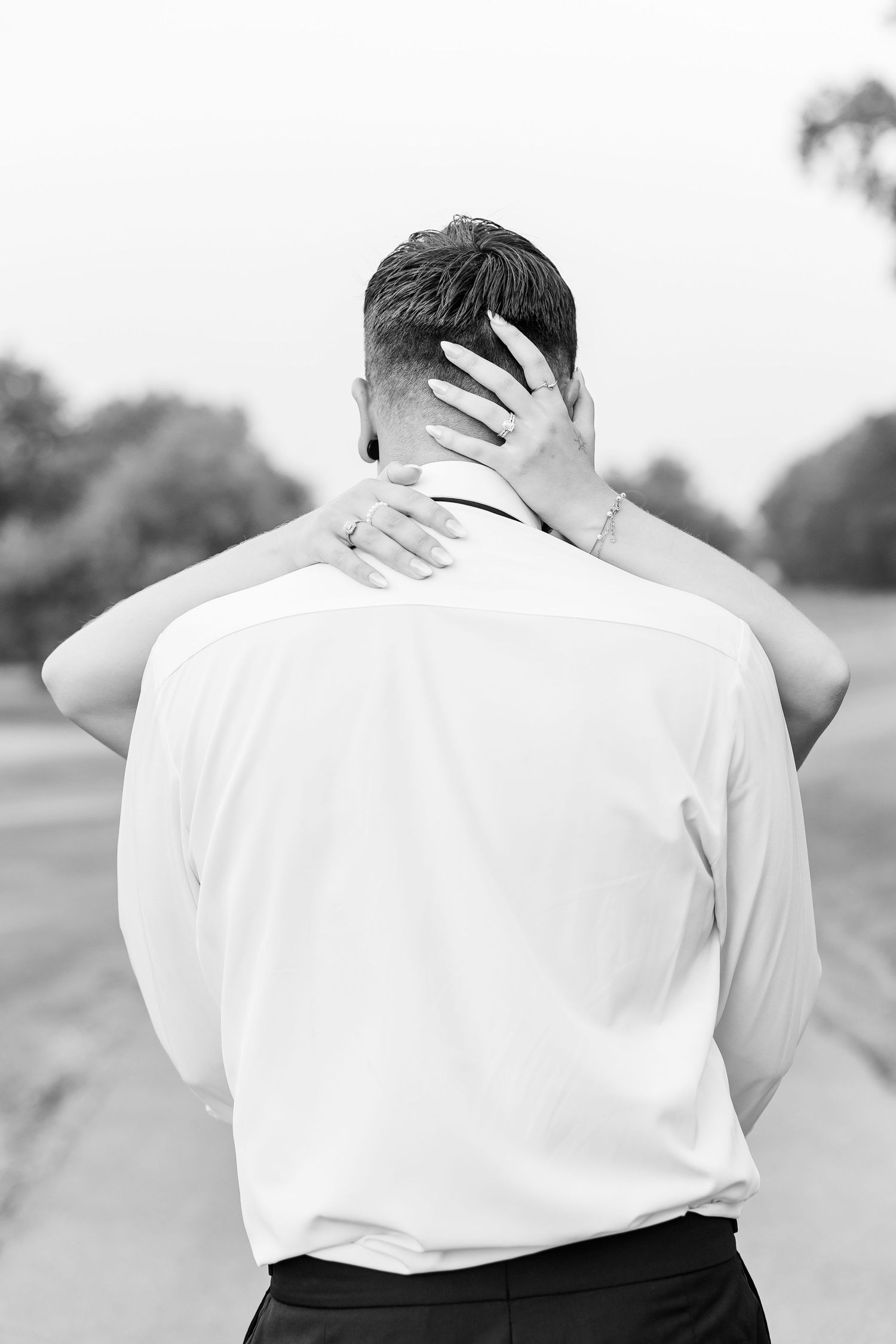Black and white photo of a couple embracing outdoors, woman's hand resting on man's neck and head.