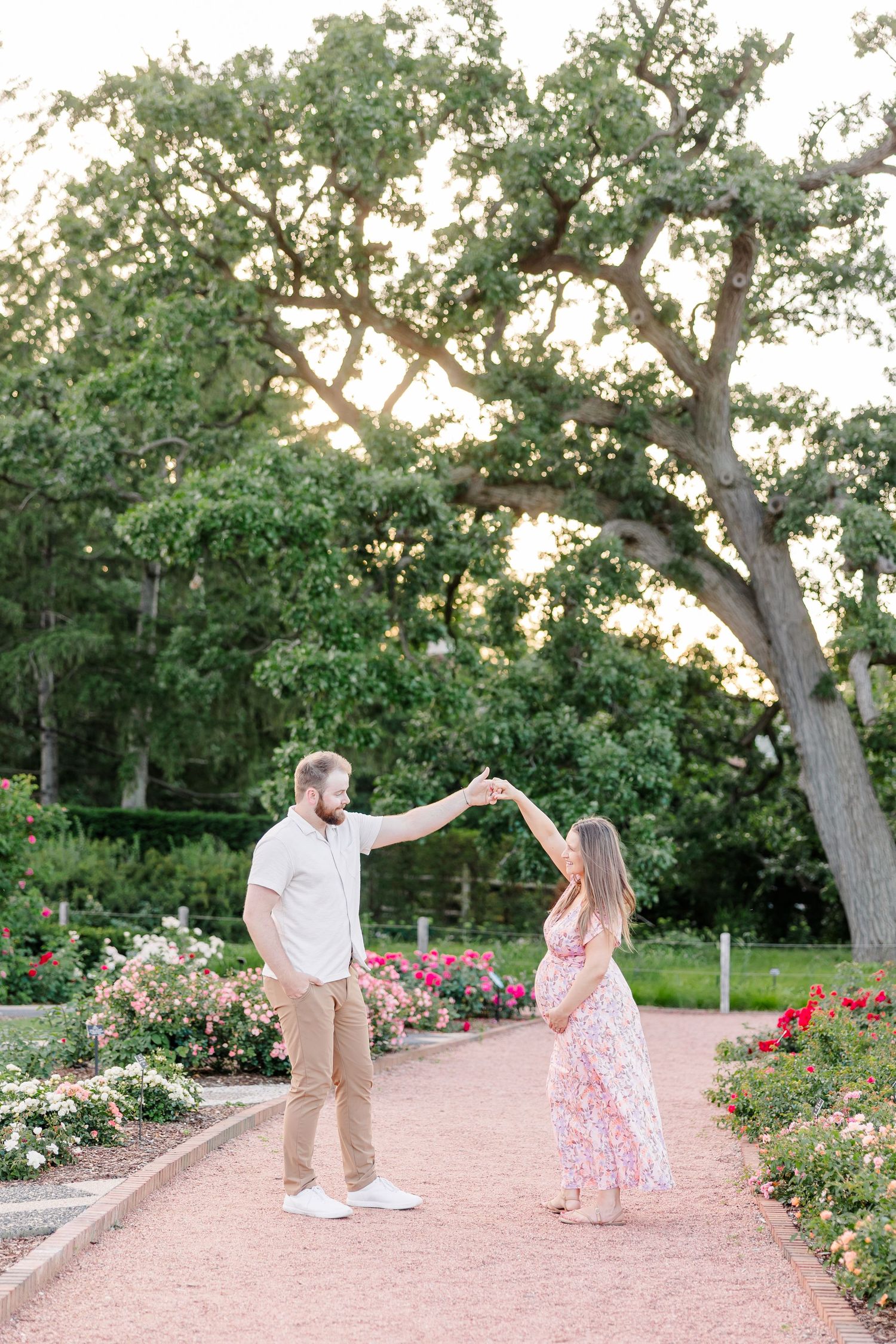 Parents-to-be walking hand in hand under a large tree during a Cantigny maternity session in Wheaton Illinois