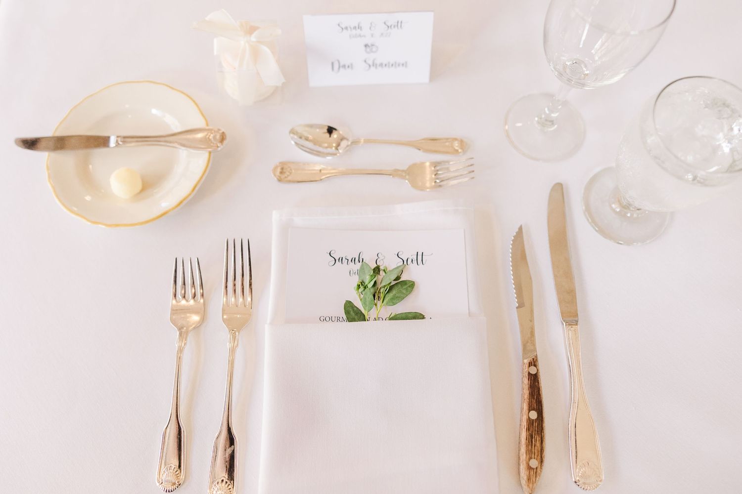 Formal place setting with gold flatware, white plates, and delicate greenery name card.