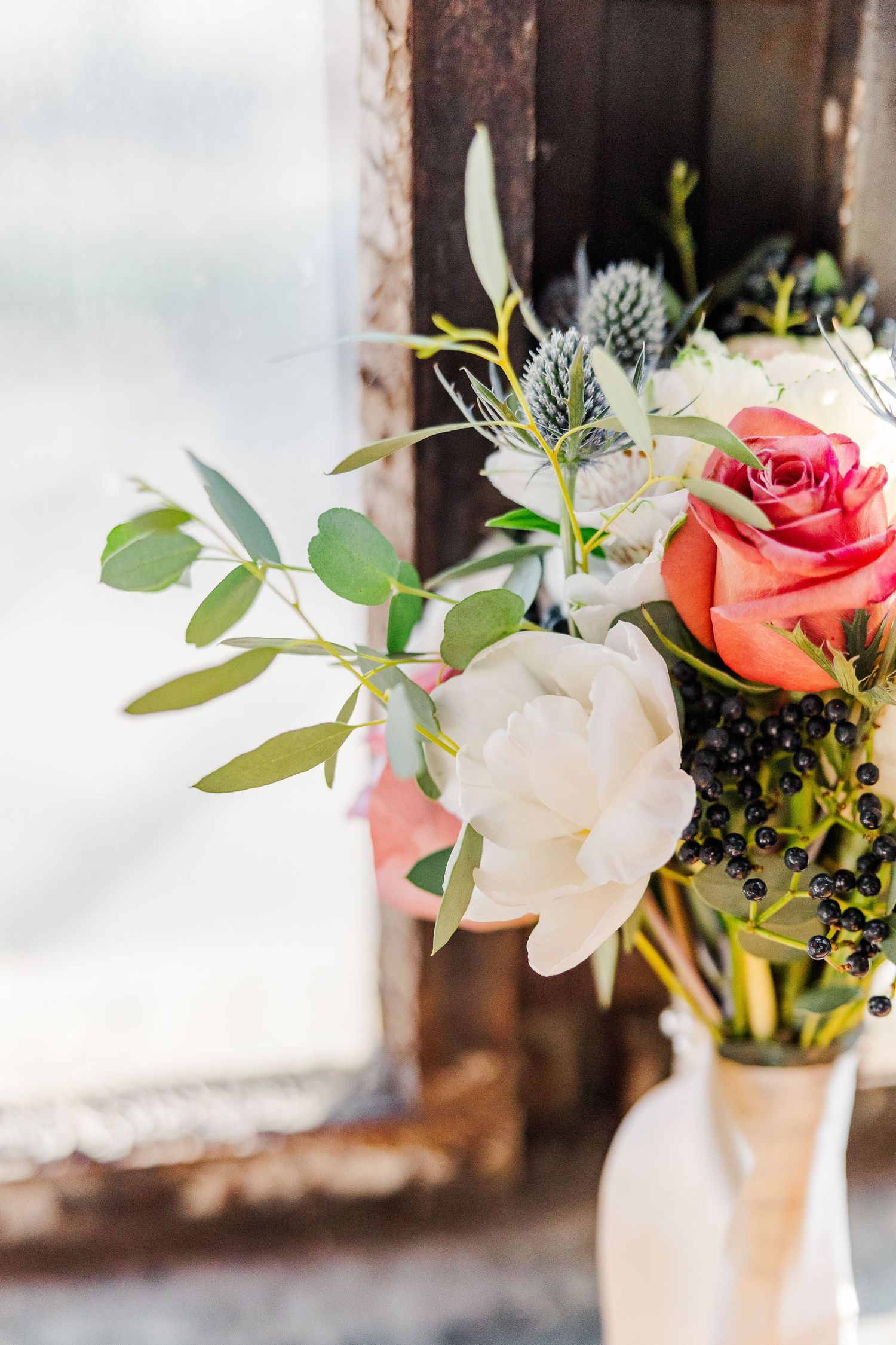 Close-up of coral rose and white floral arrangement with eucalyptus stems in a cream vase.