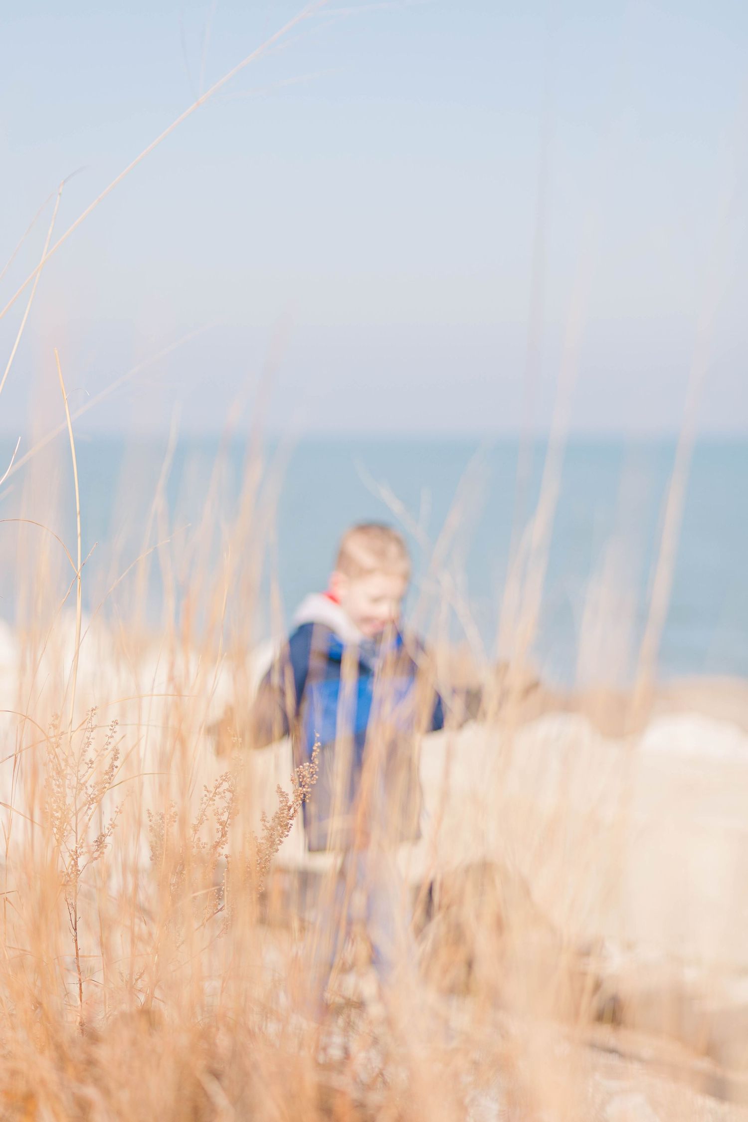 Blurred figure walking through tall beach grass with ocean in background.