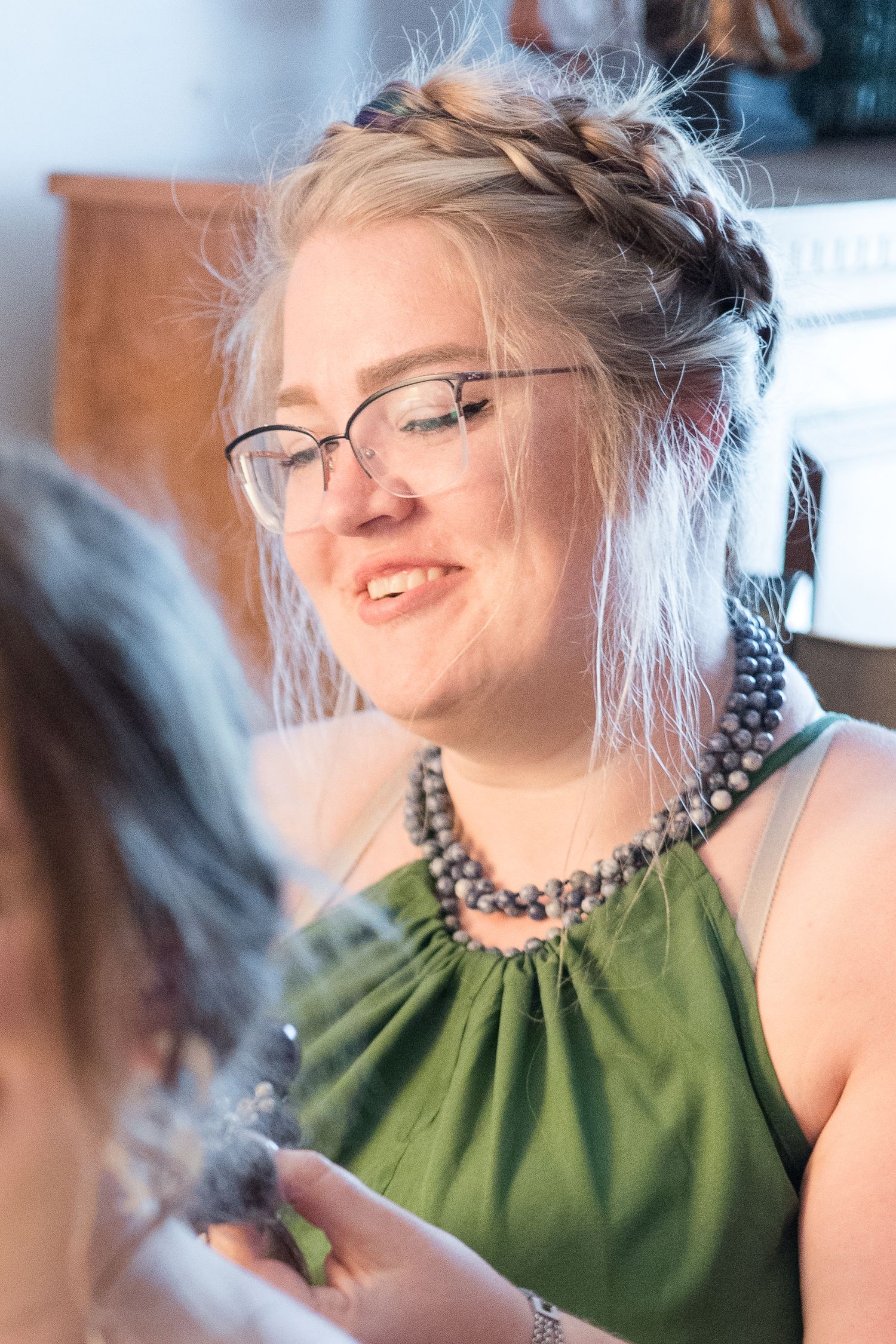 Person wearing glasses and green halter top with beaded necklace smiles during celebratory gathering.