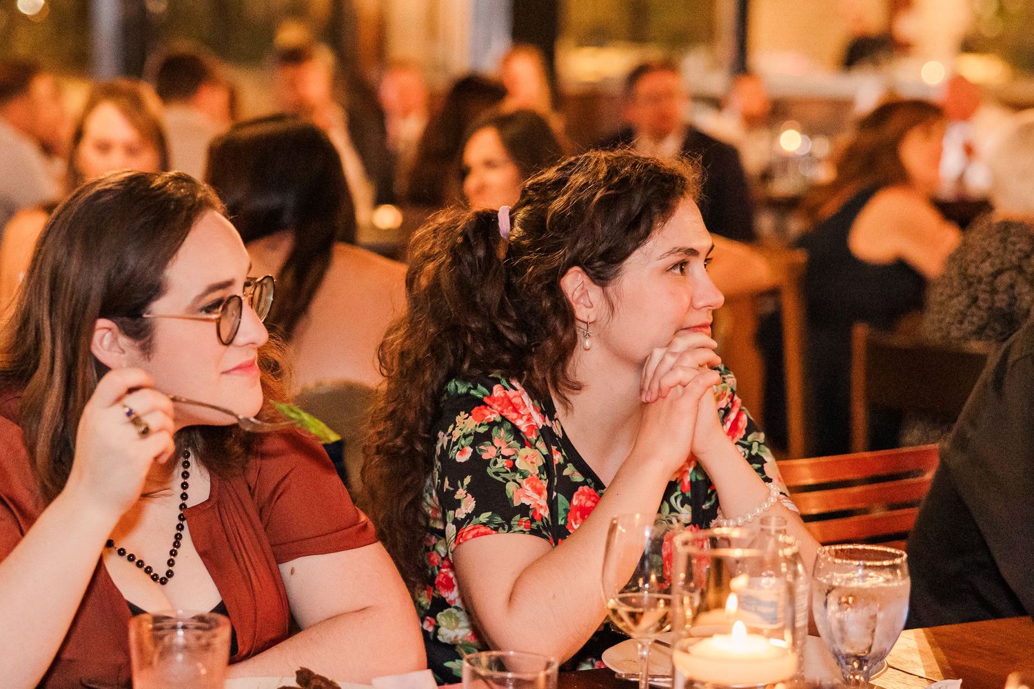 Guests attentively watch speeches during wedding reception in warm candlelit venue.