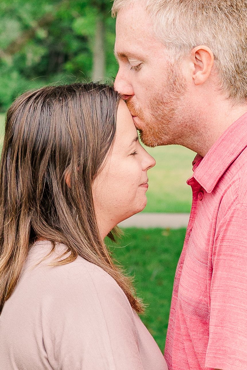 An intimate moment between a couple as they share a gentle forehead kiss in a garden setting.
