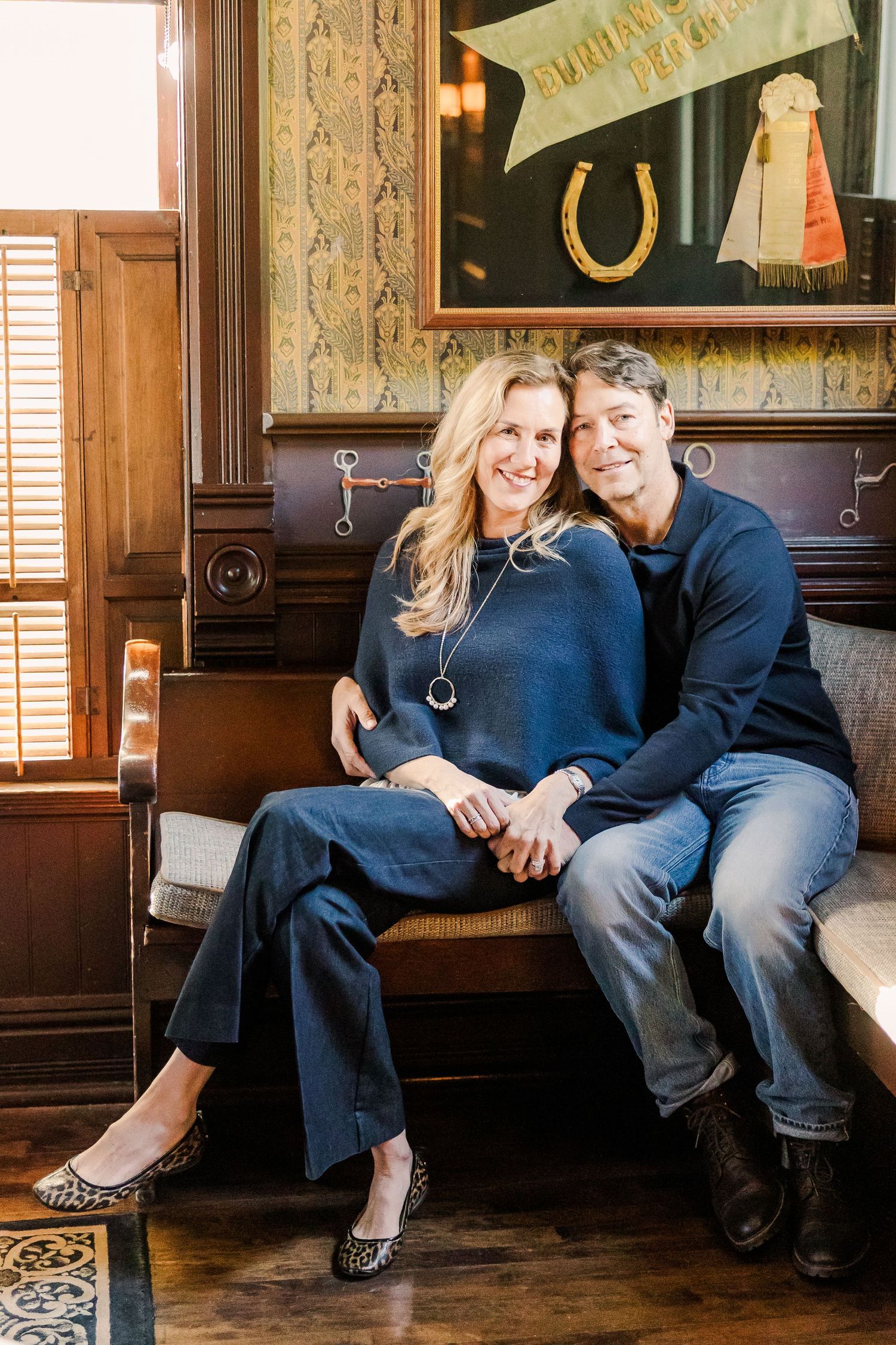 A couple sits close together on an antique bench in a room with vintage decor.
