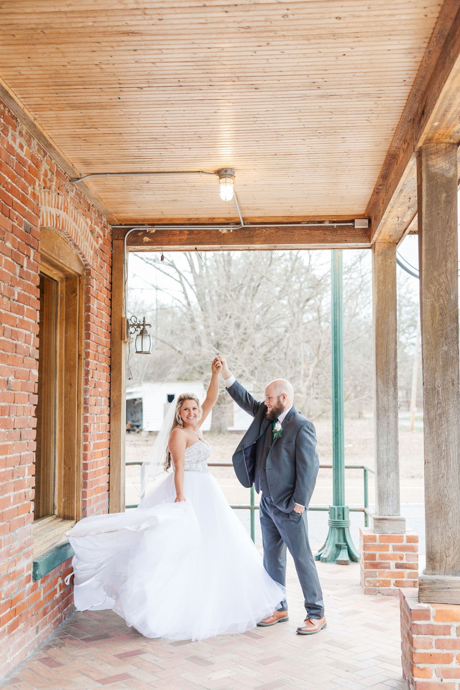 Happy couple celebrates on a covered porch as they raise their joined hands in joy.