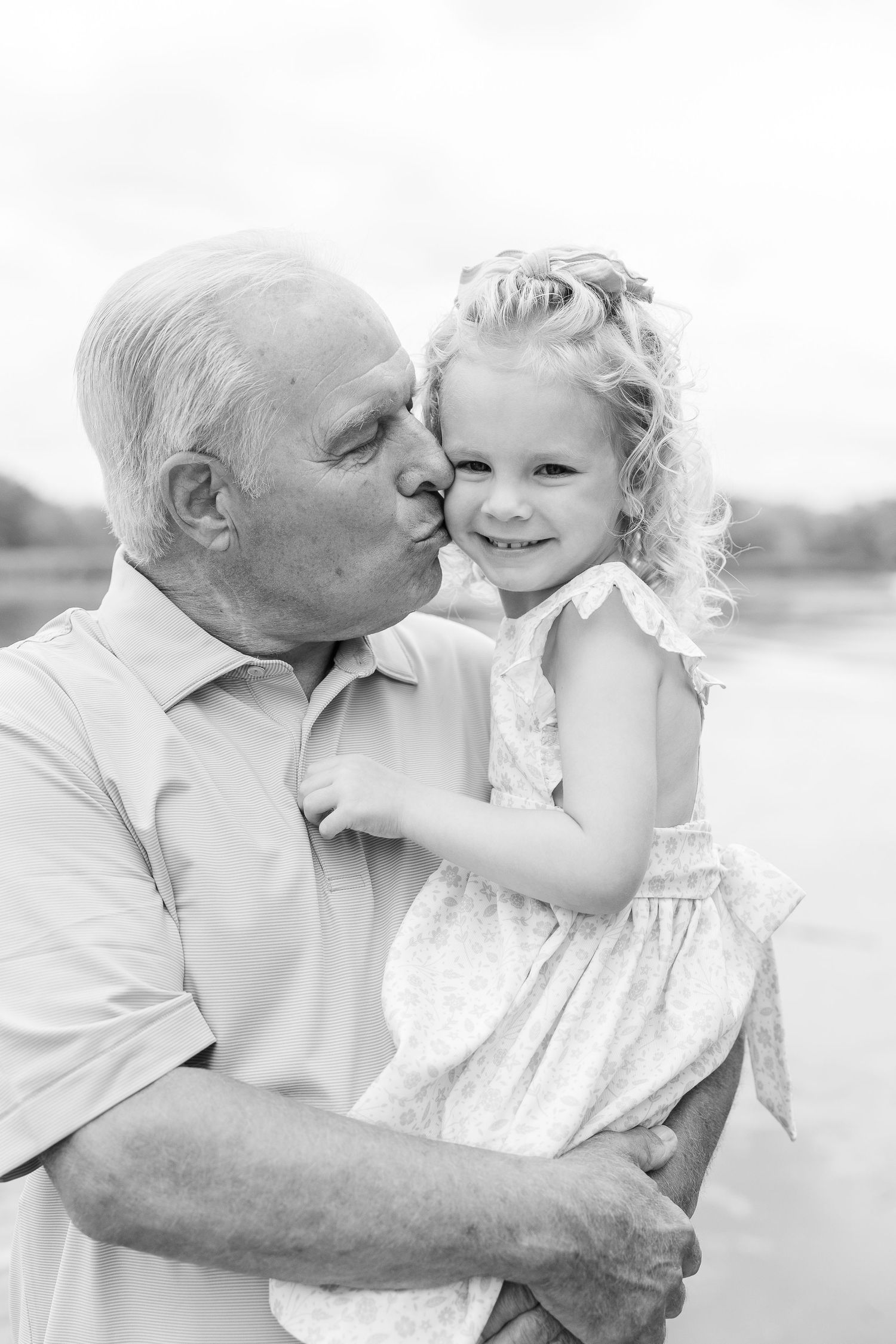 A tender black and white portrait of an elder sharing a sweet moment with a young child by the water.