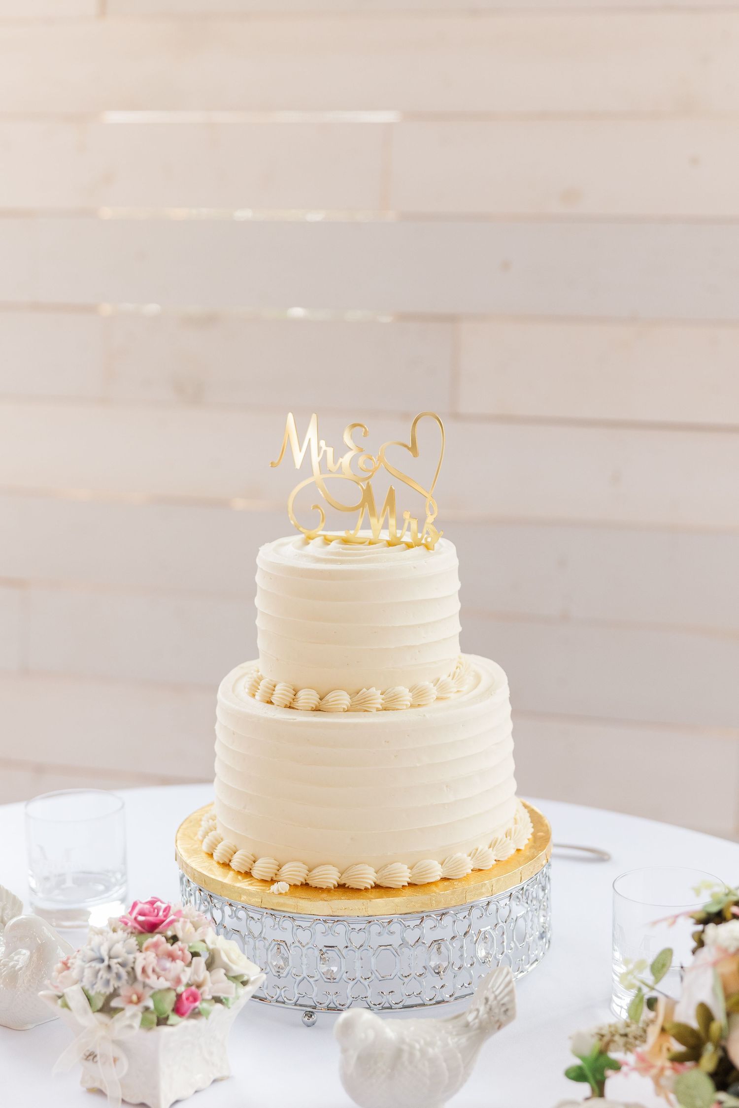 Classic white tiered wedding cake with gold accents and Mr & Mrs topper on silver stand.