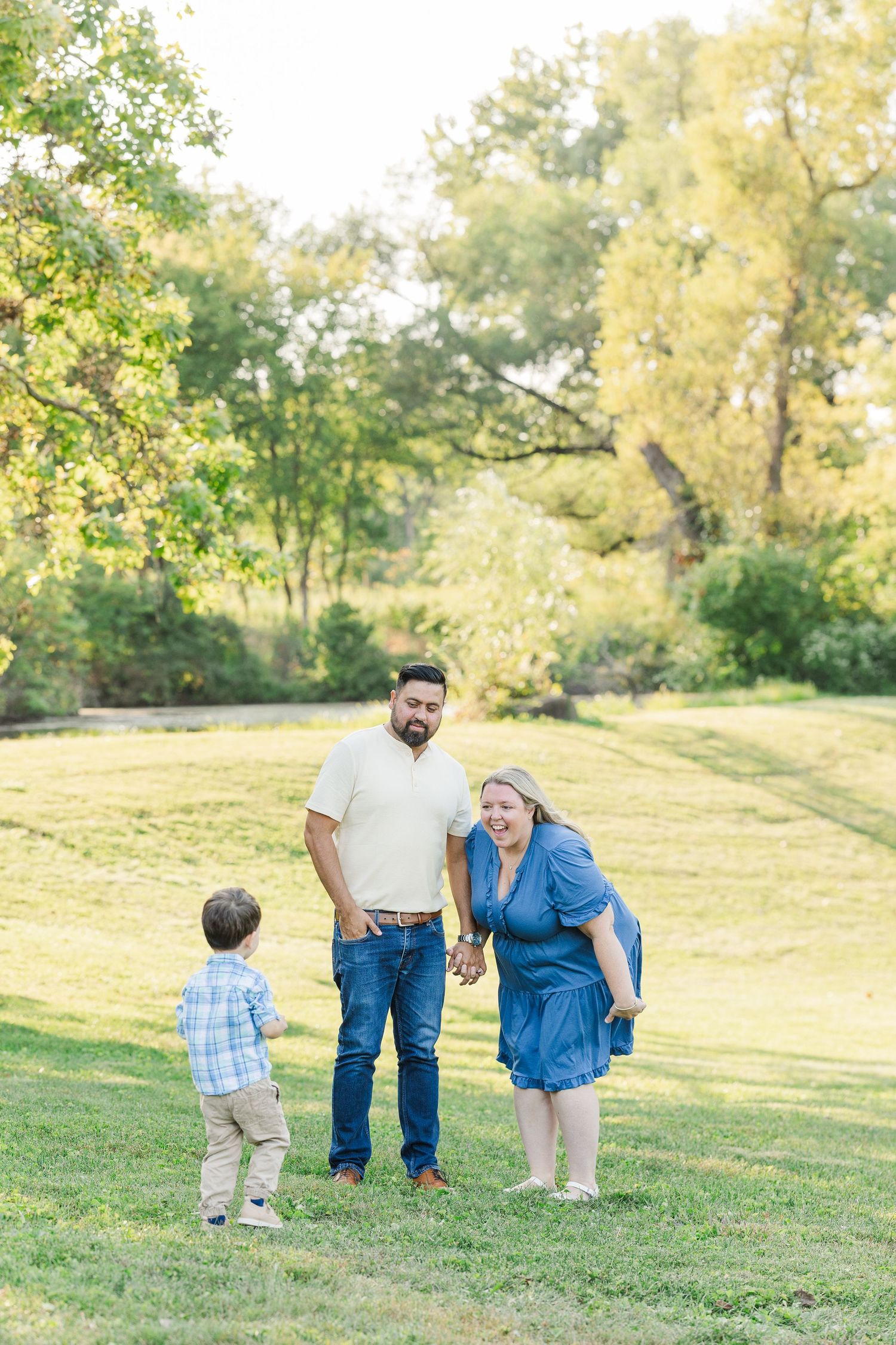 Little one takes first steps in grassy hillside park during a bright golden sunset while learning to walk.Sorg family portraits at Shamrock