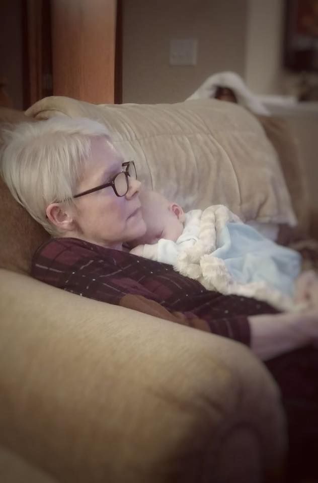 Person sleeping peacefully on a couch with a light blanket in a dimly lit room.