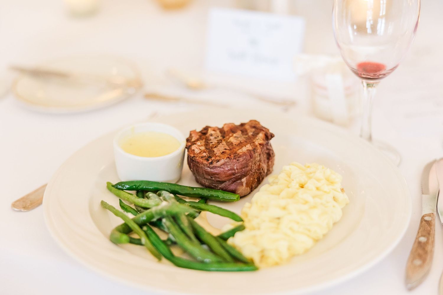 Plated dinner with filet mignon, green beans, and mashed potatoes on white china.