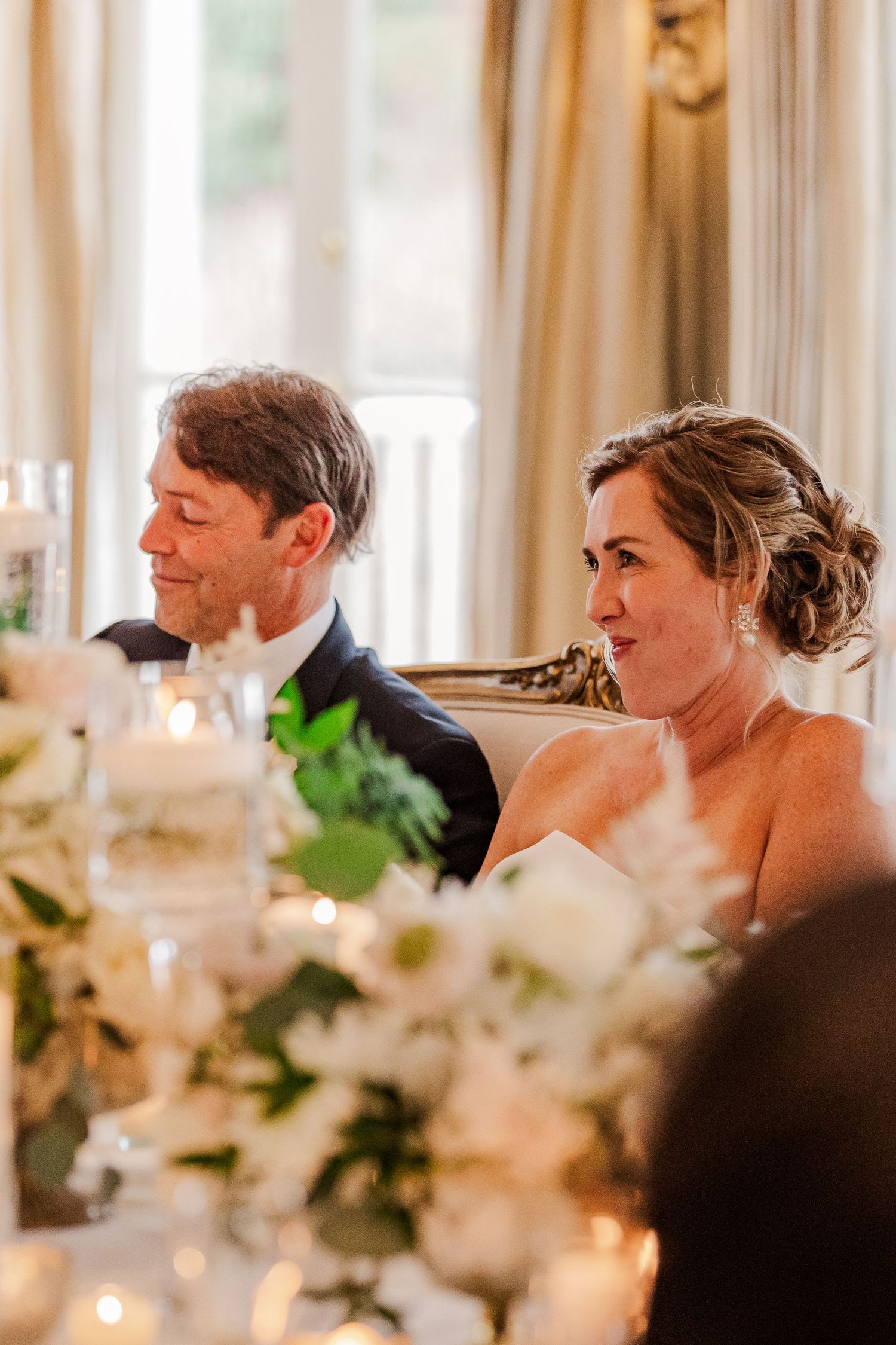 Wedding reception moment captured during speeches at elegant venue with floral decorations.