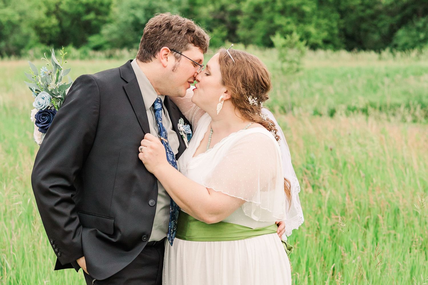 Newlyweds share an intimate moment while standing in a grassy meadow.