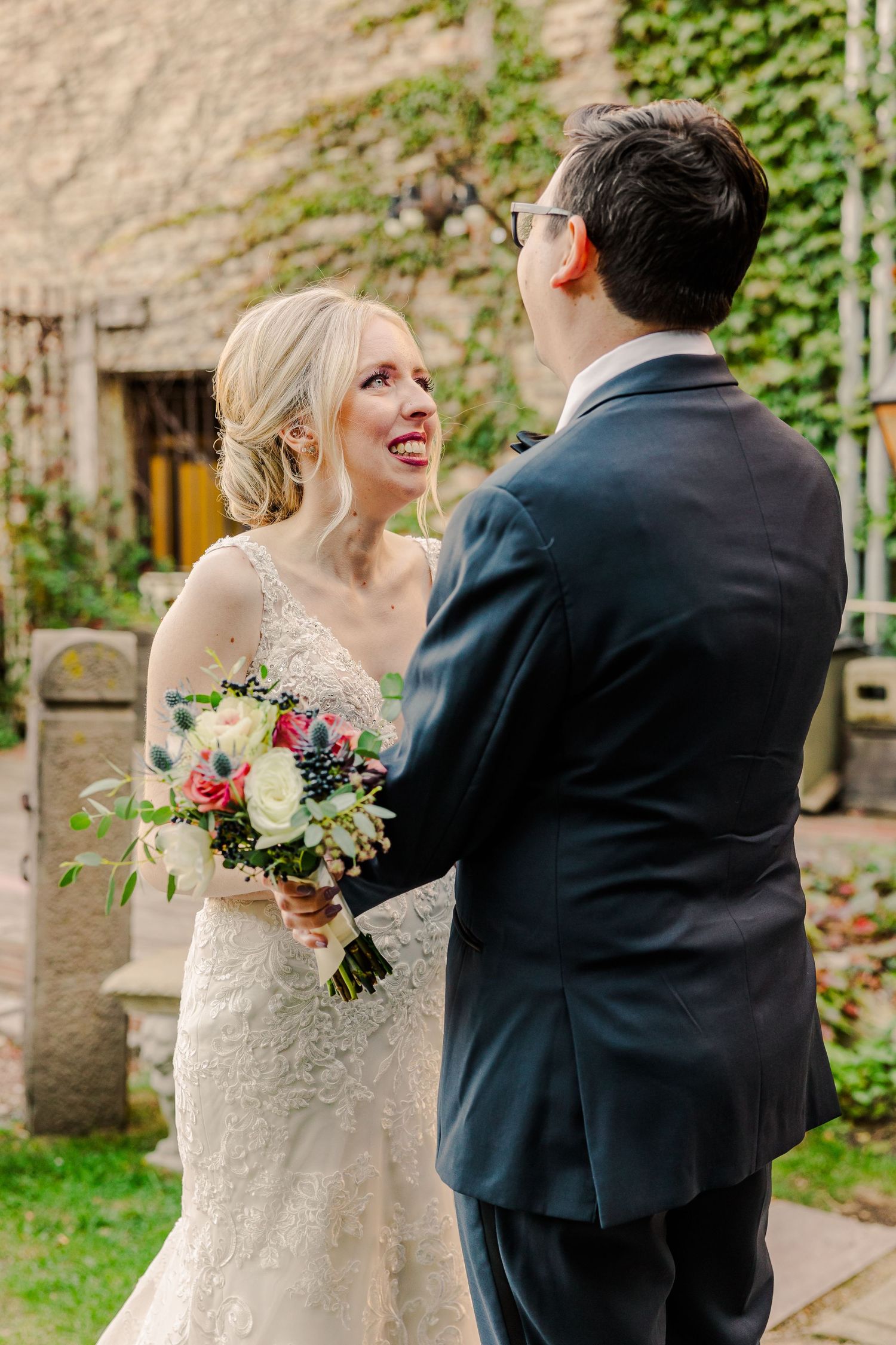 Candid wedding moment with couple exchanging smiles while holding floral bouquet.