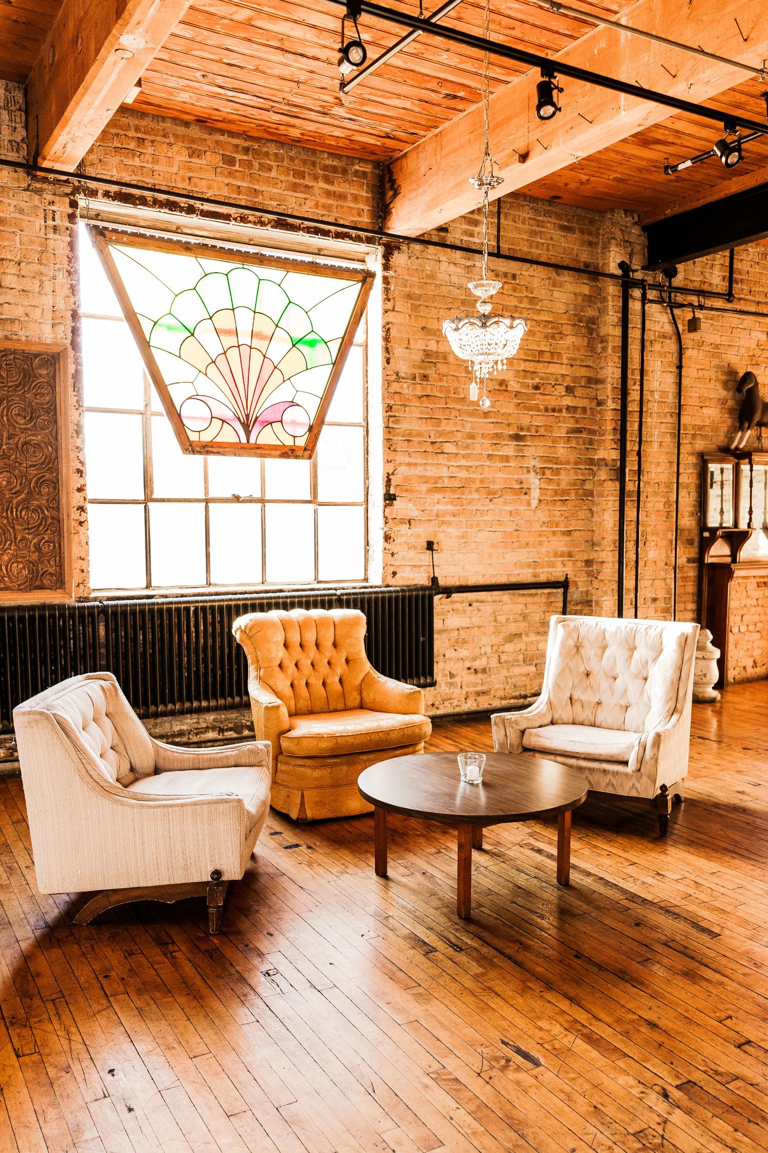 Elegant vintage lounge area with tufted chairs, exposed brick walls, hardwood floors and stained glass window detail.