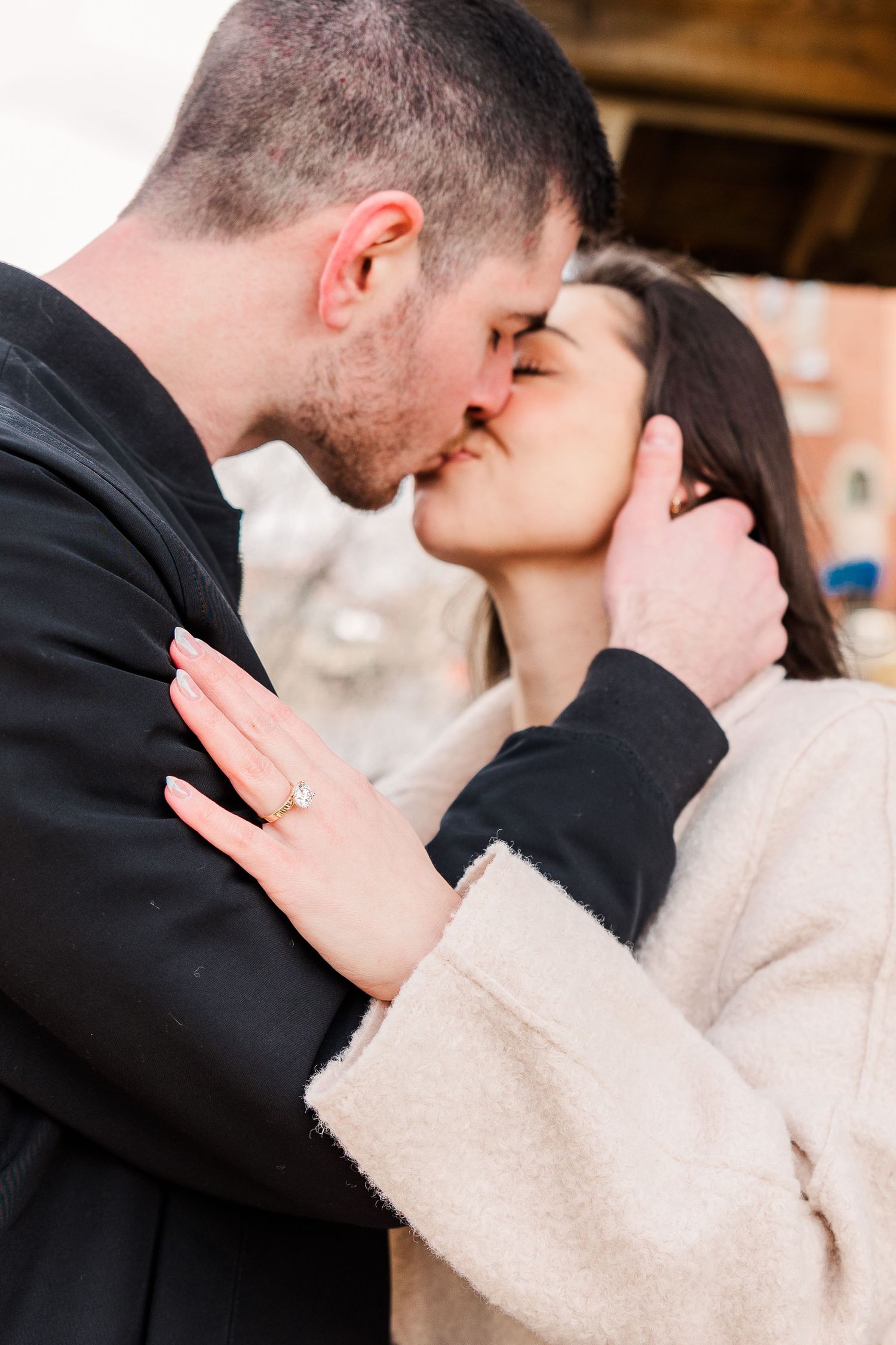An intimate engagement photo showing a couple embracing while displaying a ring.
