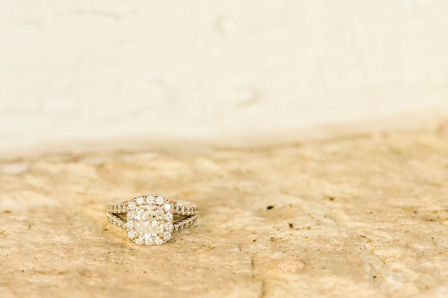An elegant diamond engagement ring photographed on a textured beige stone surface.