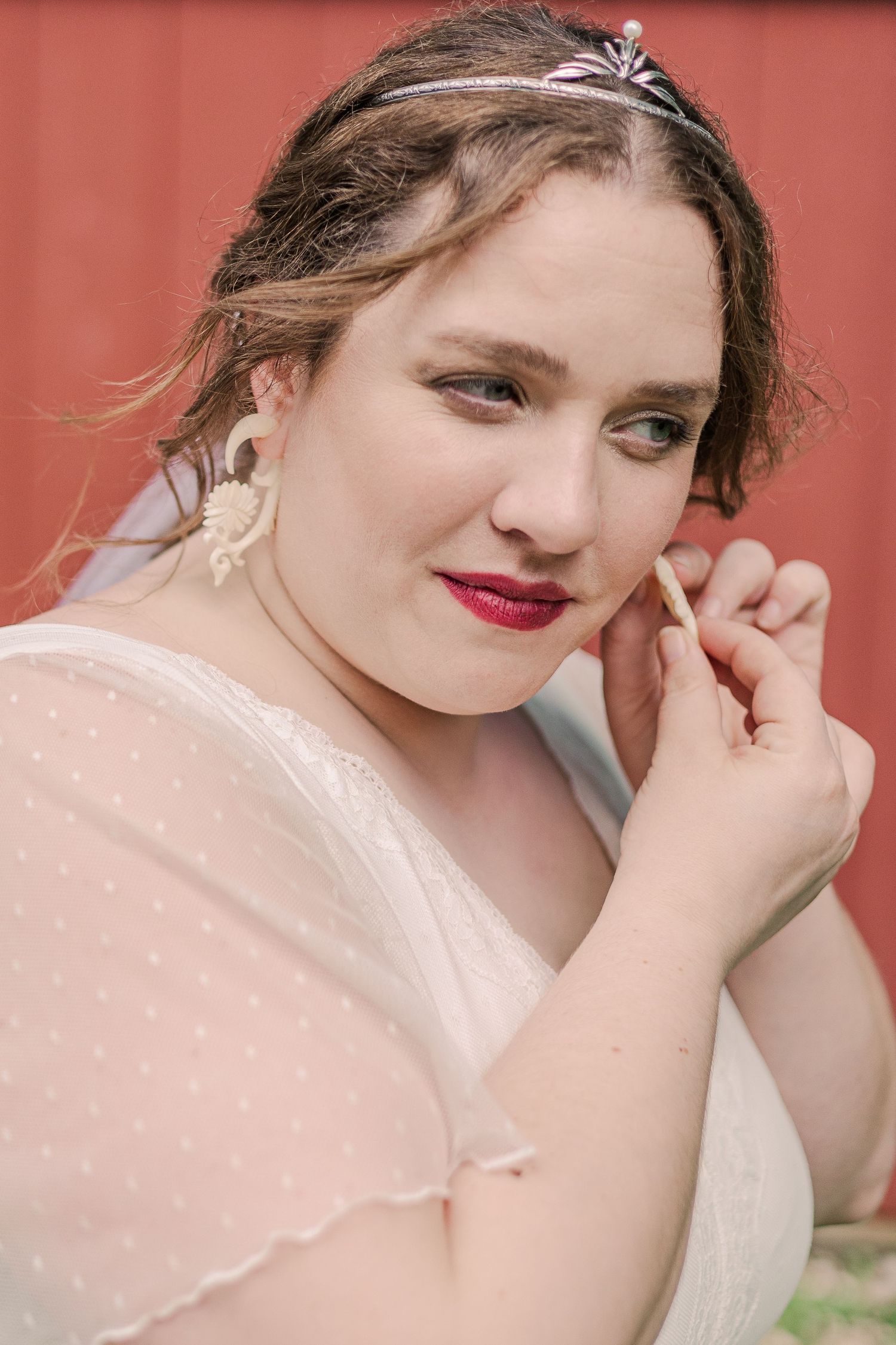Close portrait of person wearing bridal accessories and bold red lipstick.
