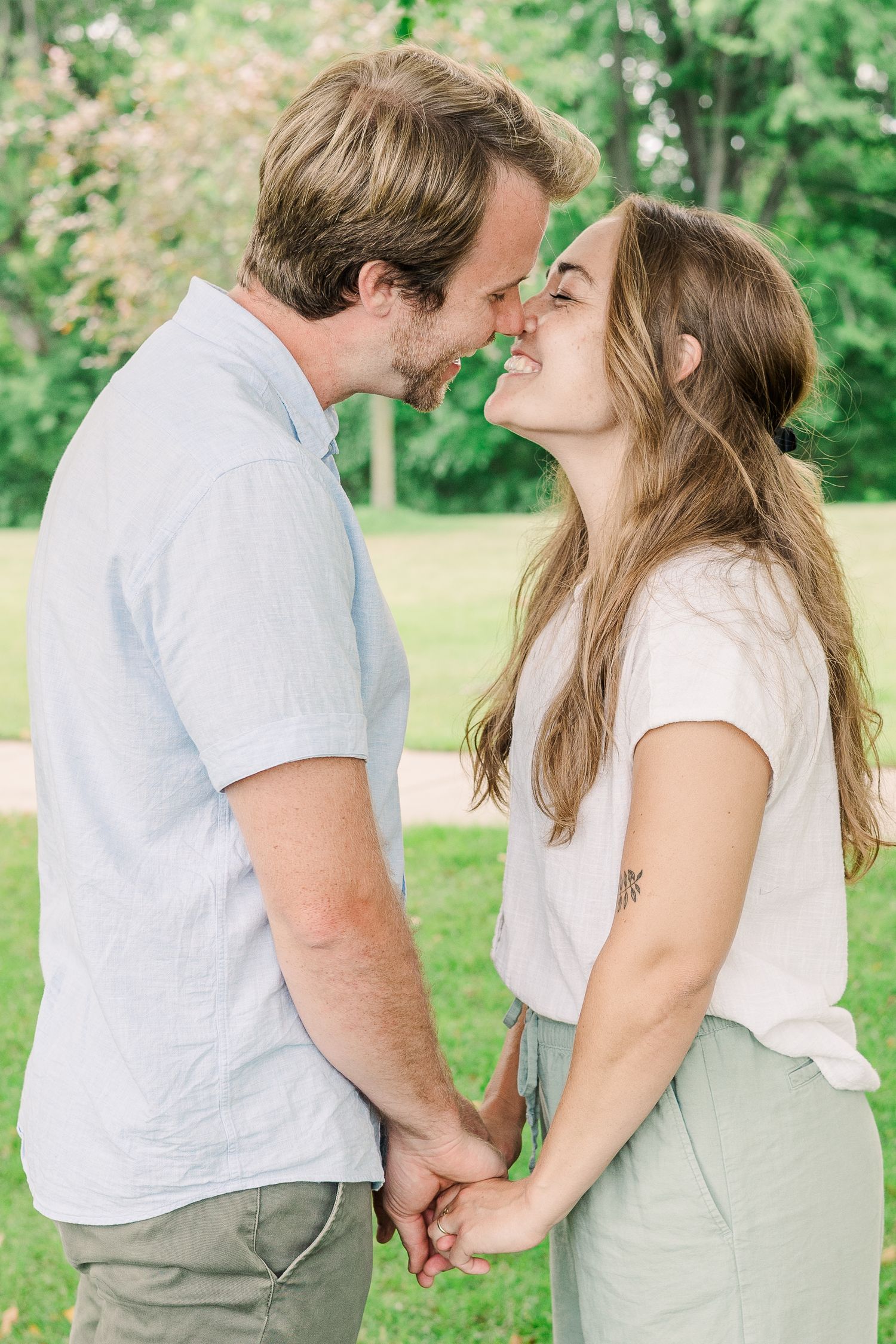 A couple shares an intimate moment while holding hands and smiling at each other in a park setting.