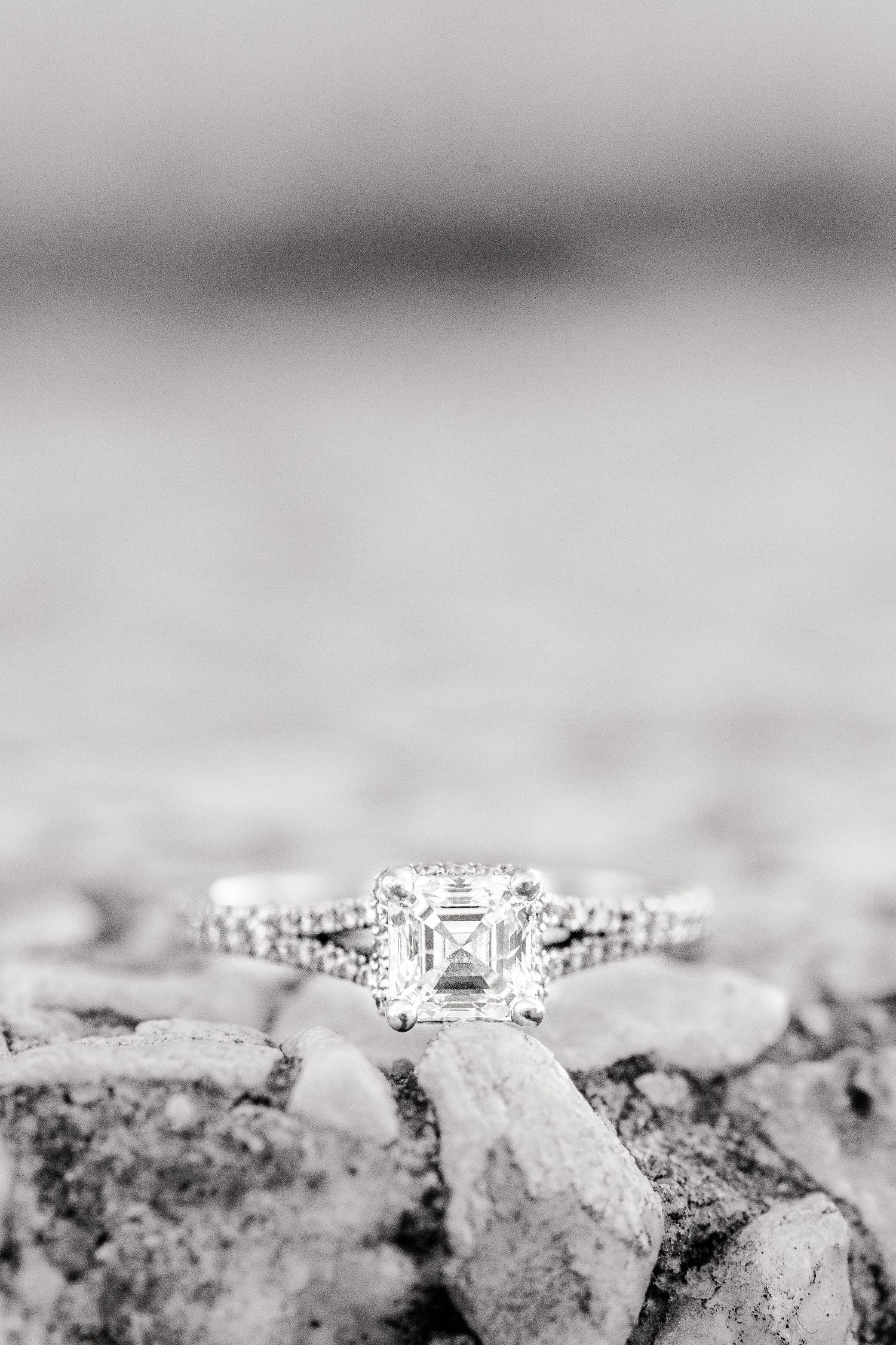A sparkling diamond engagement ring with an asscher cut center stone rests on a textured surface.