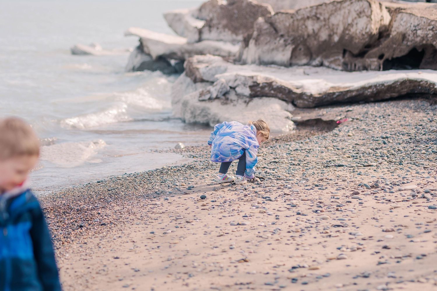 Children exploring rocky beach with driftwood and pebbles near water.