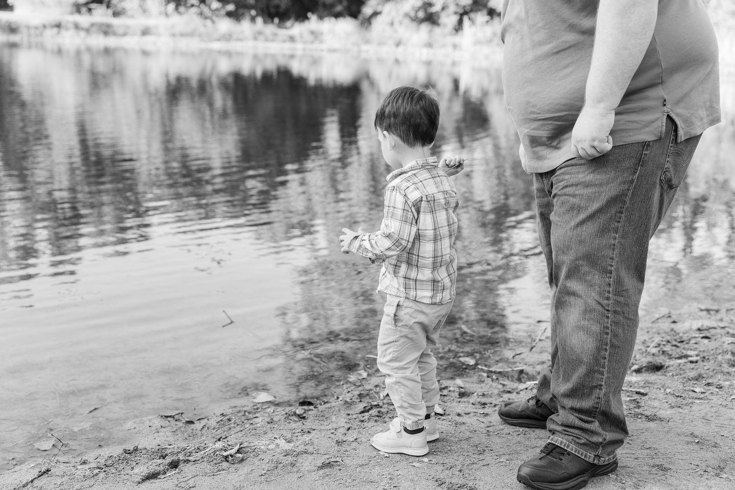 Family walks near the edge of a serene lake with their reflections cast in the still water.Sorg family portraits at Shamrock Hills Park in C