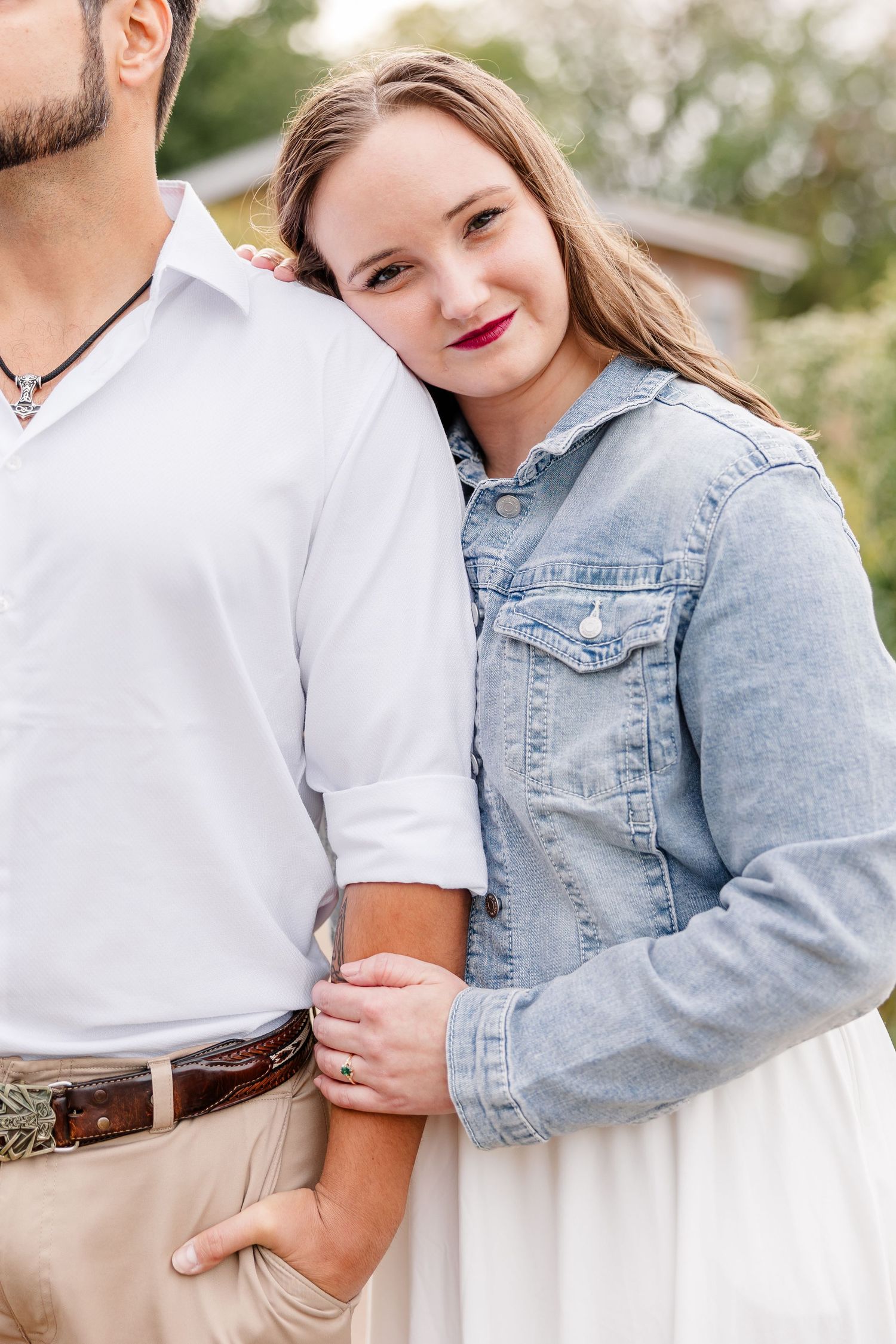 Smiling woman in a denim jacket rests her head on a man's shoulder during an outdoor couple portrait session.