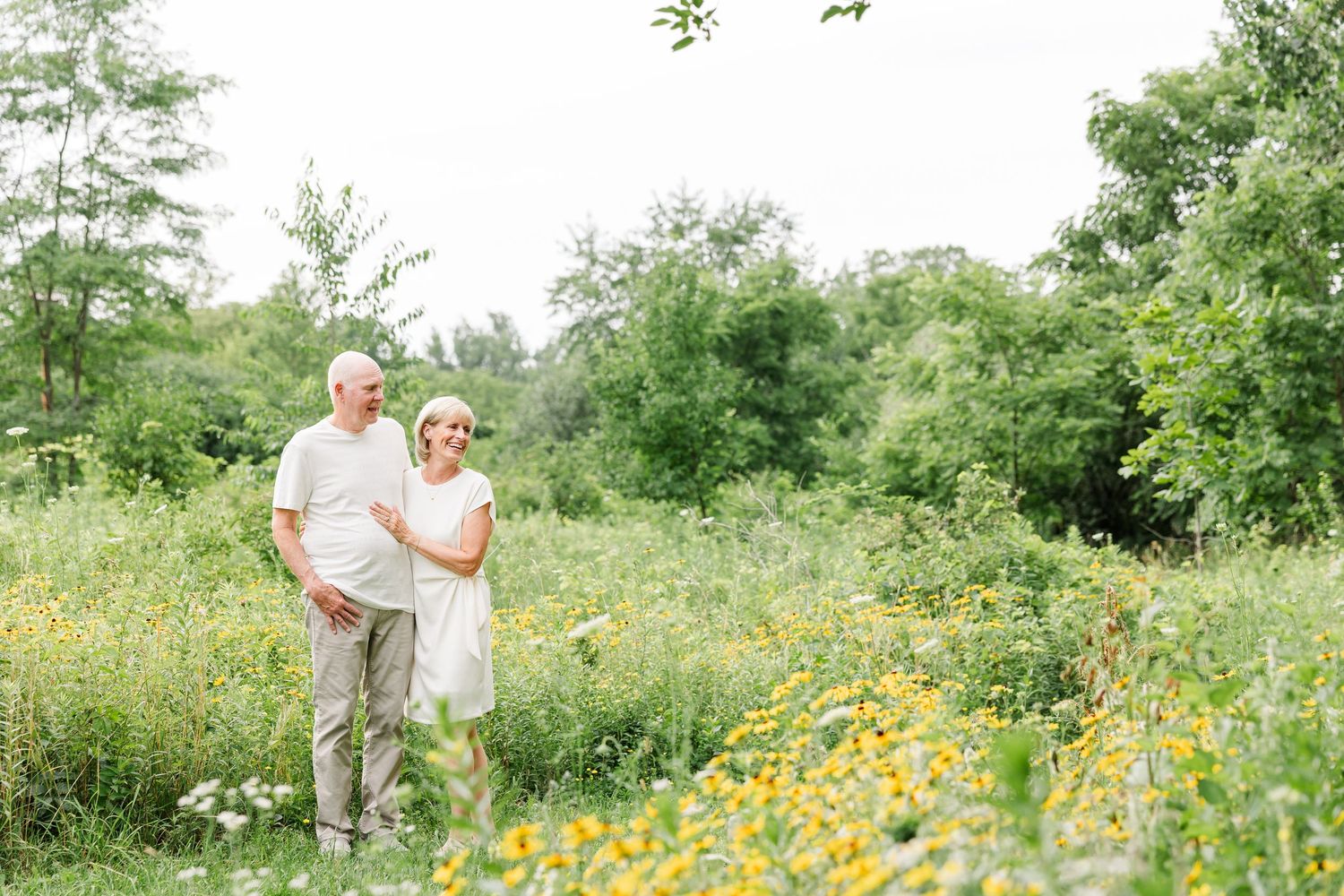Elderly couple walking hand in hand through a lush green meadow with yellow wildflowers.
