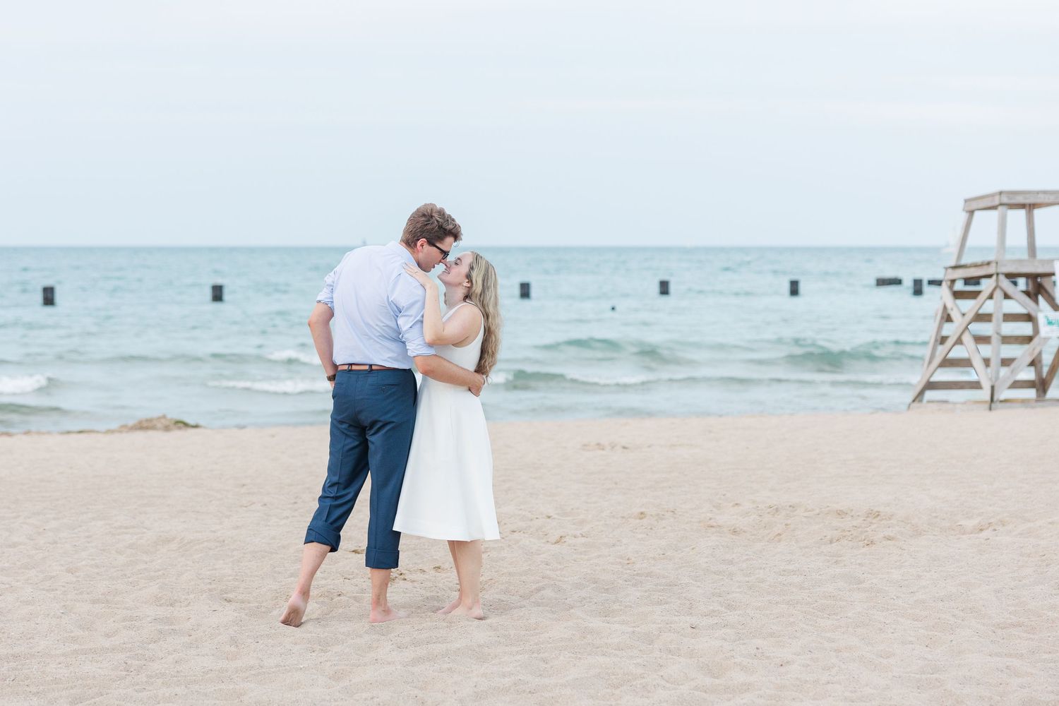 Elizabeth and Joe kissing along North Avenue Beach, with gentle waves and a soft sunset in the background