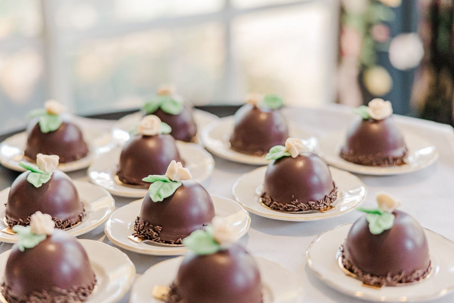 Chocolate dome desserts decorated with mint leaves arranged on small white plates.