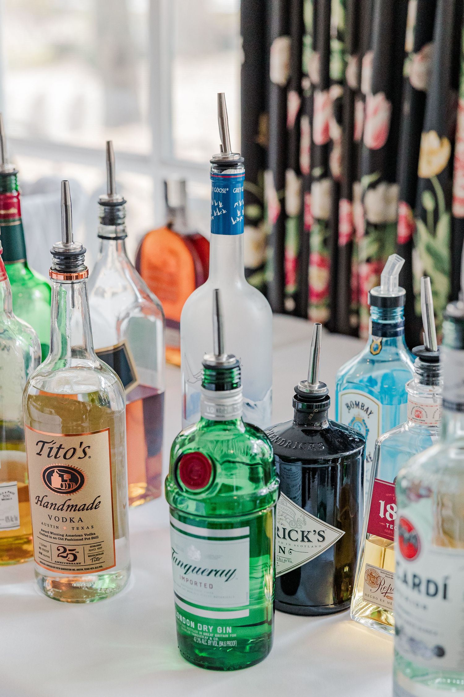 Assorted liquor bottles including Tito's vodka and gin arranged on a white surface.