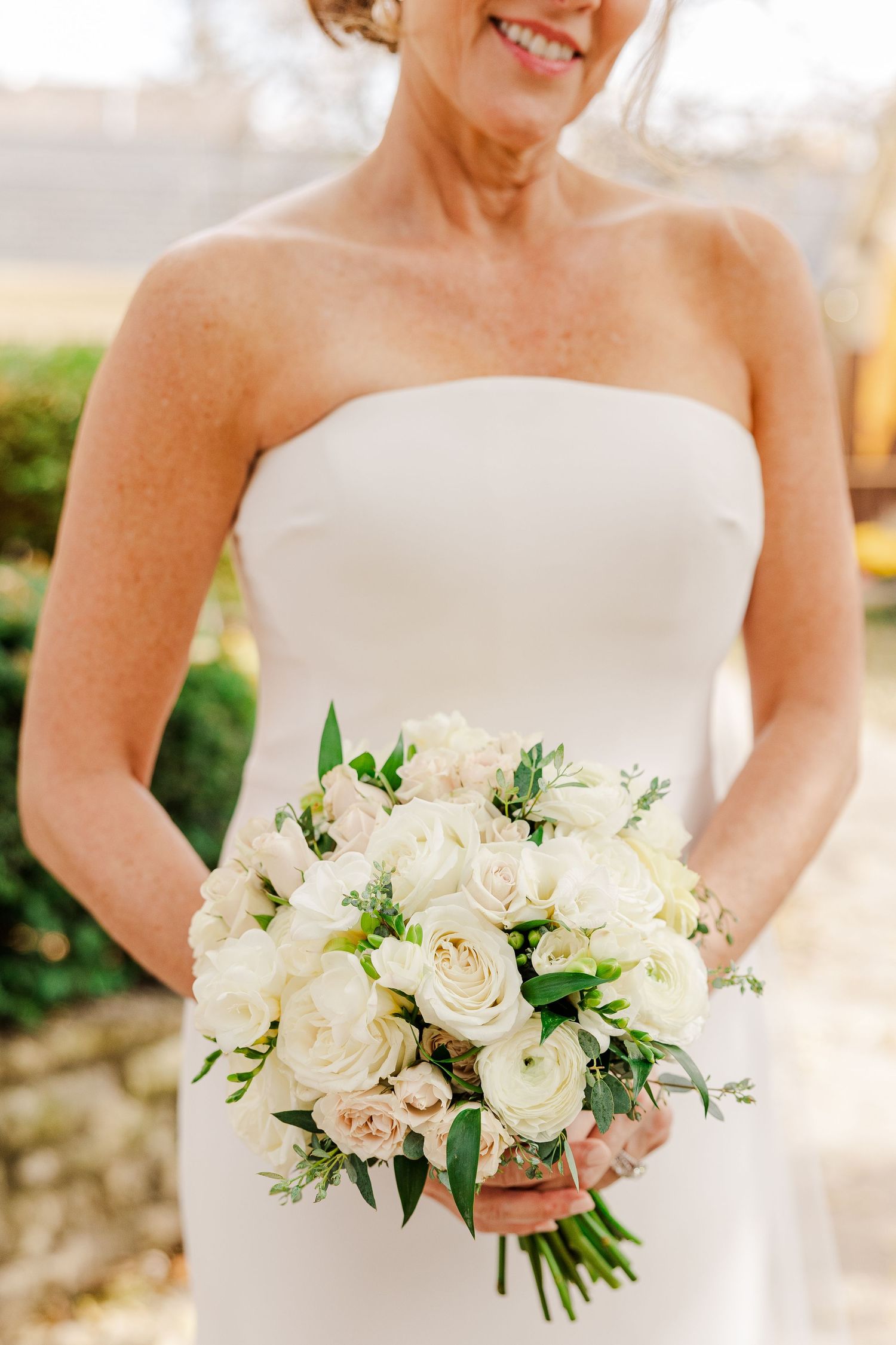 Classic white bridal bouquet with roses and greenery against natural light.