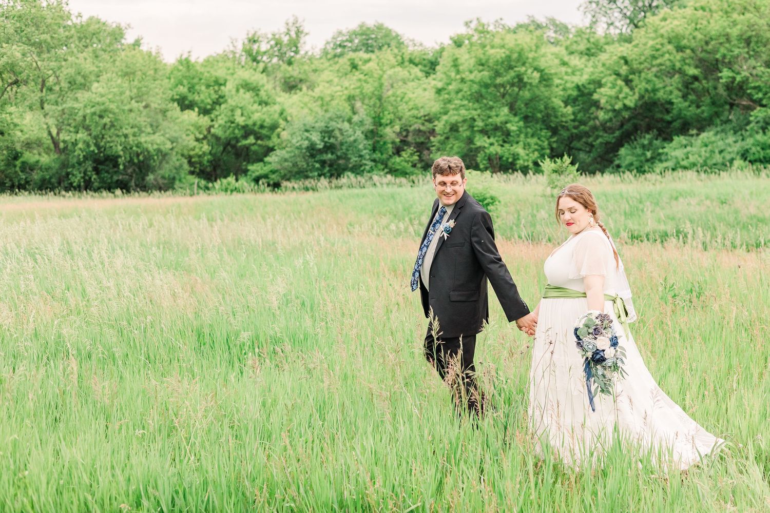 A dreamy wedding photo of newlyweds walking through a sunlit meadow with spring flowers.