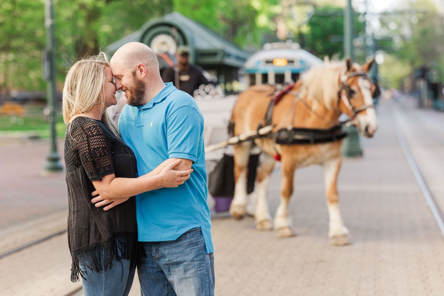 A couple embraces on a street with a horse-drawn carriage in the background.