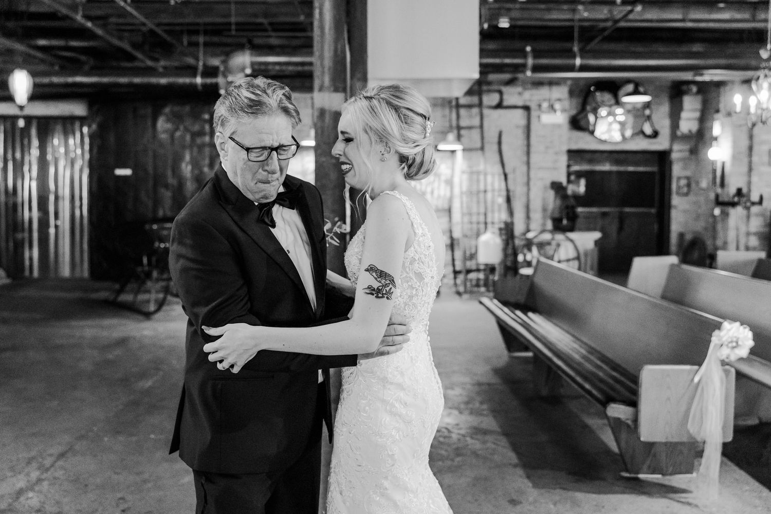 A black and white photograph capturing a tender dance moment at an industrial-style wedding venue.