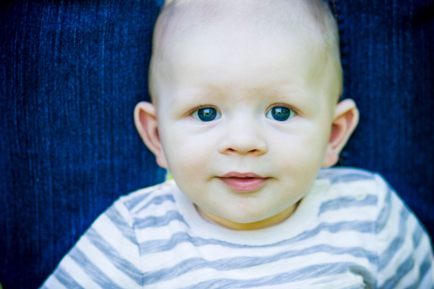 Close up portrait of an infant wearing a gray and white striped shirt.