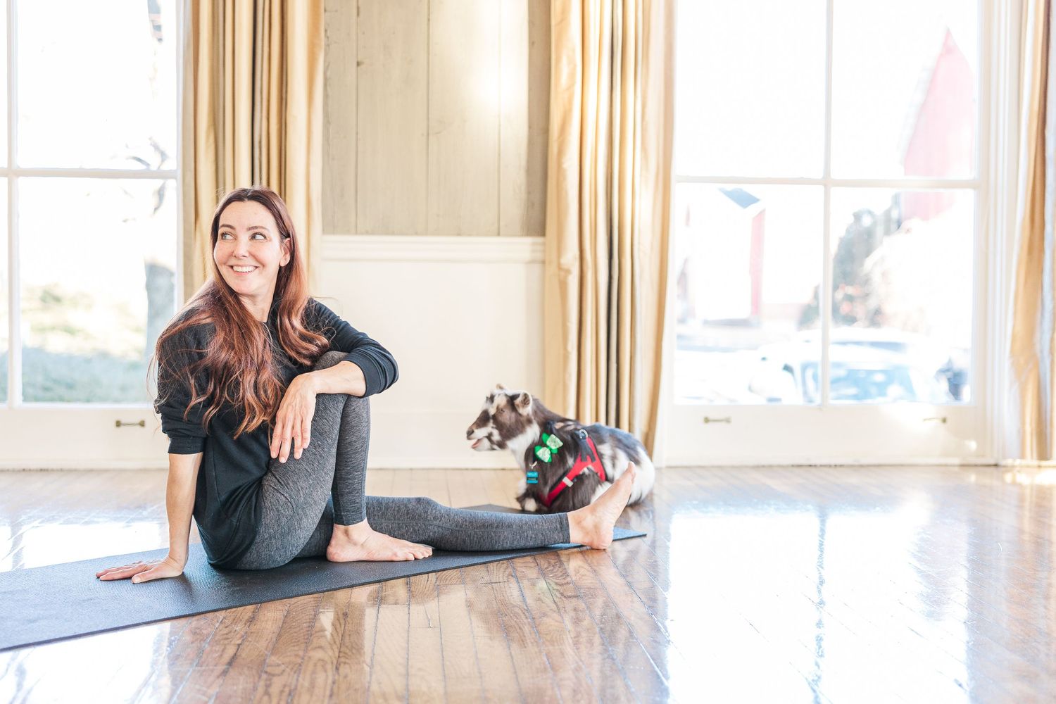 A yoga participant takes a rest position on a blue mat in a sunny studio space.