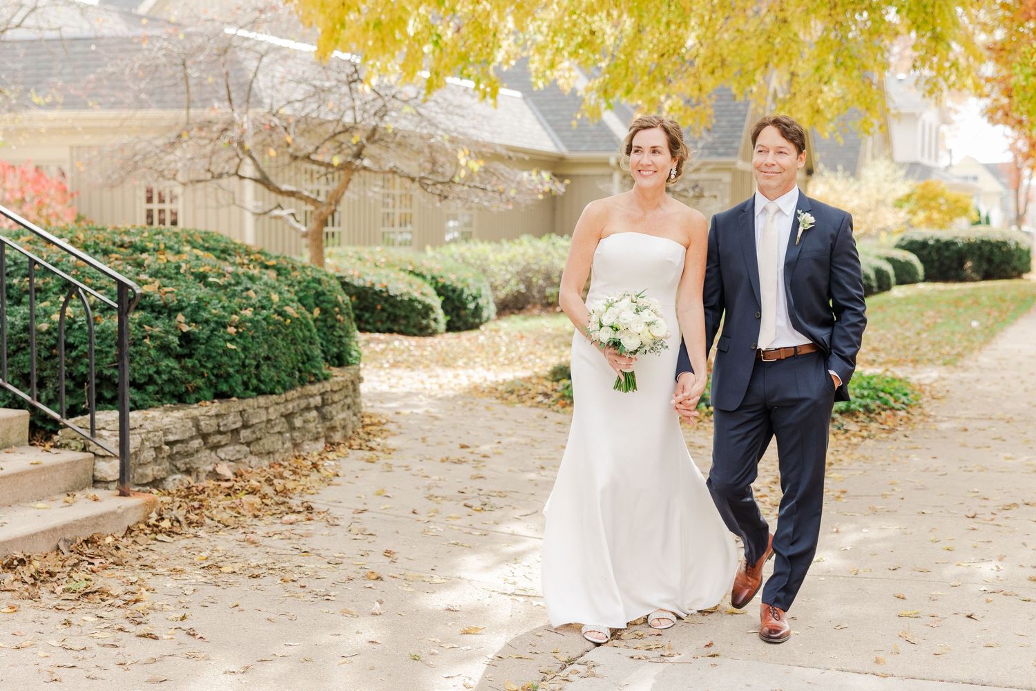 A cheerful wedding photo on stone steps with fall foliage in the background.
