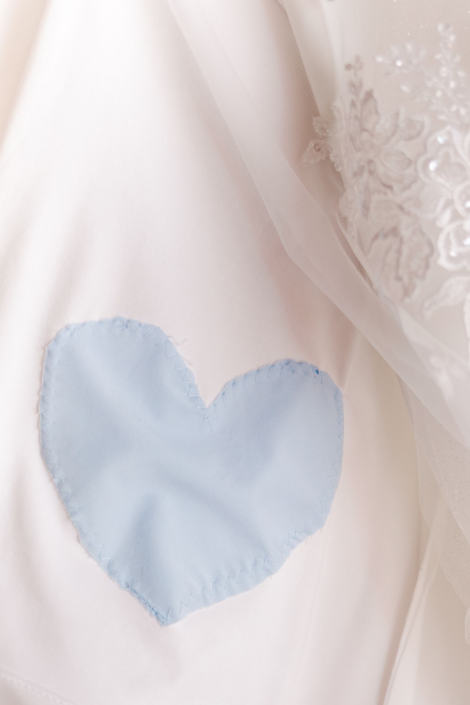 Light blue heart patch sewn onto white fabric with delicate lace overlay.