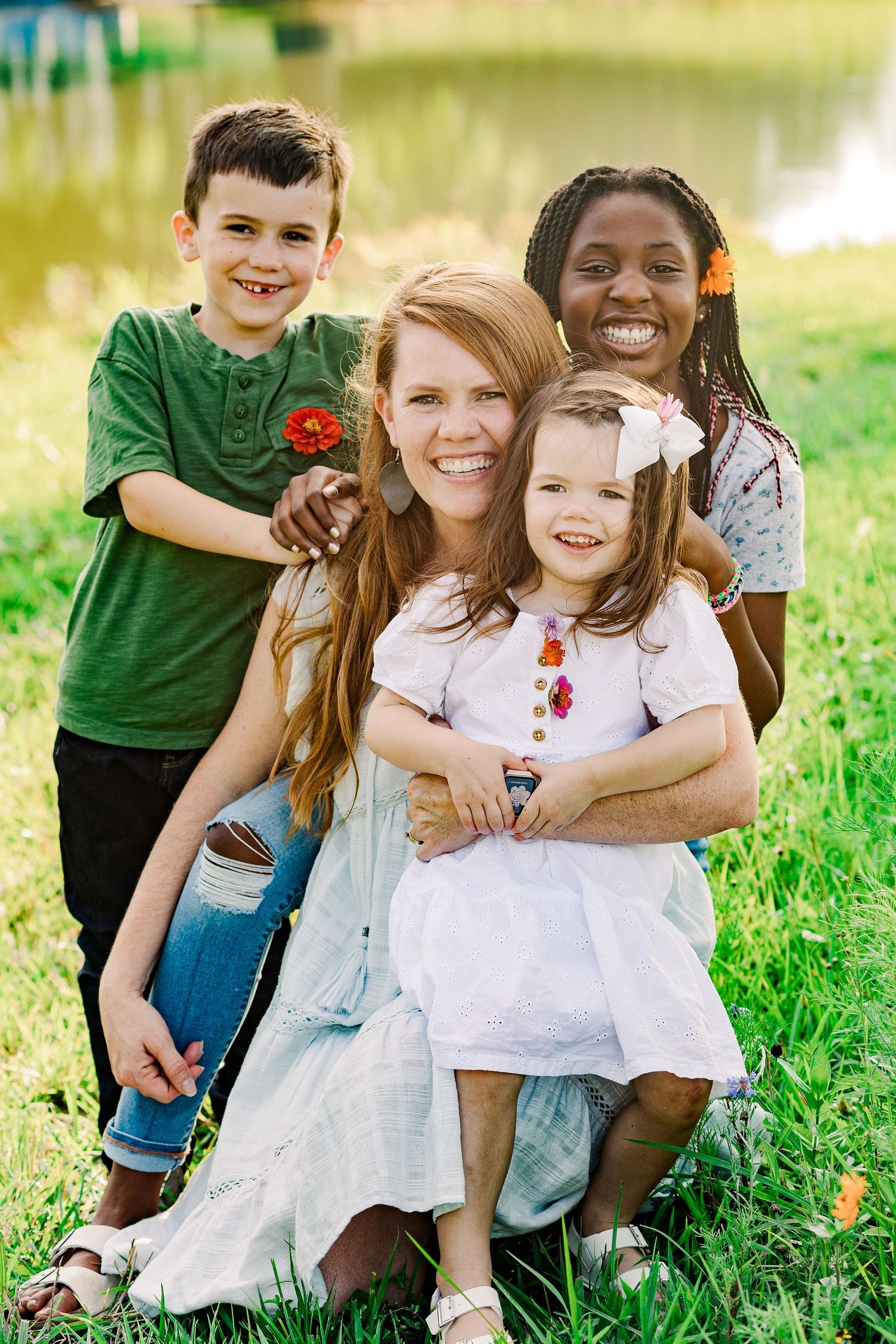 Family sitting together on grass near a pond on a bright sunny day.