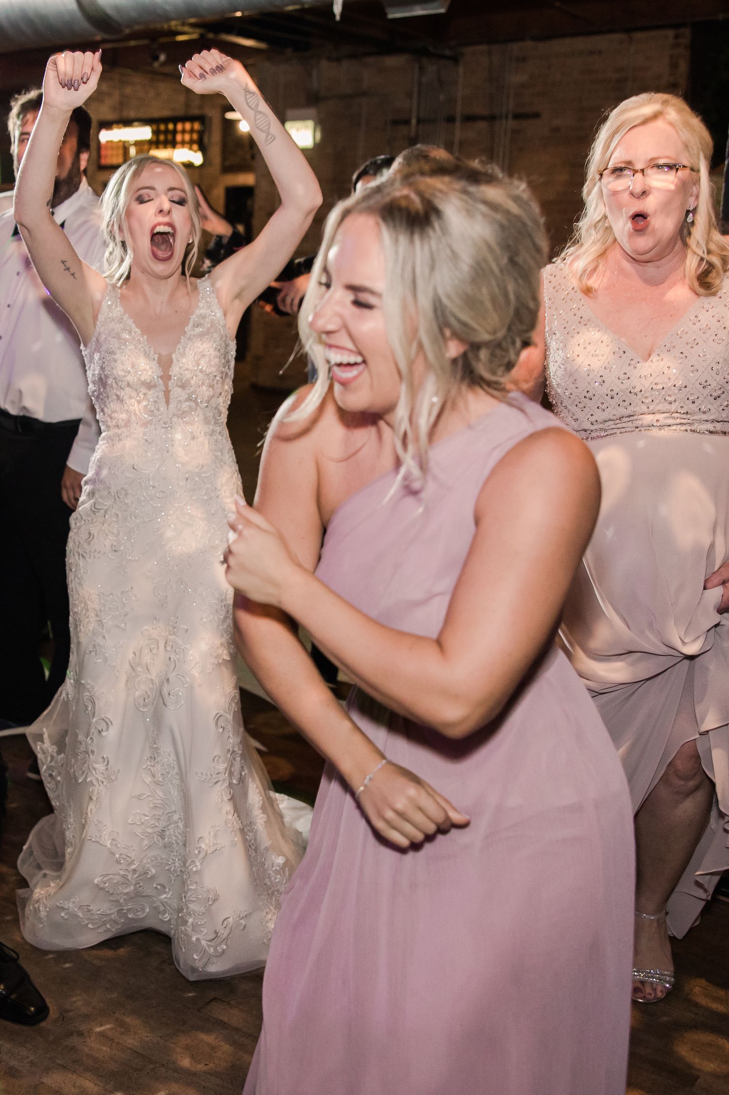 Wedding celebration with guests dancing and celebrating on wooden dance floor.