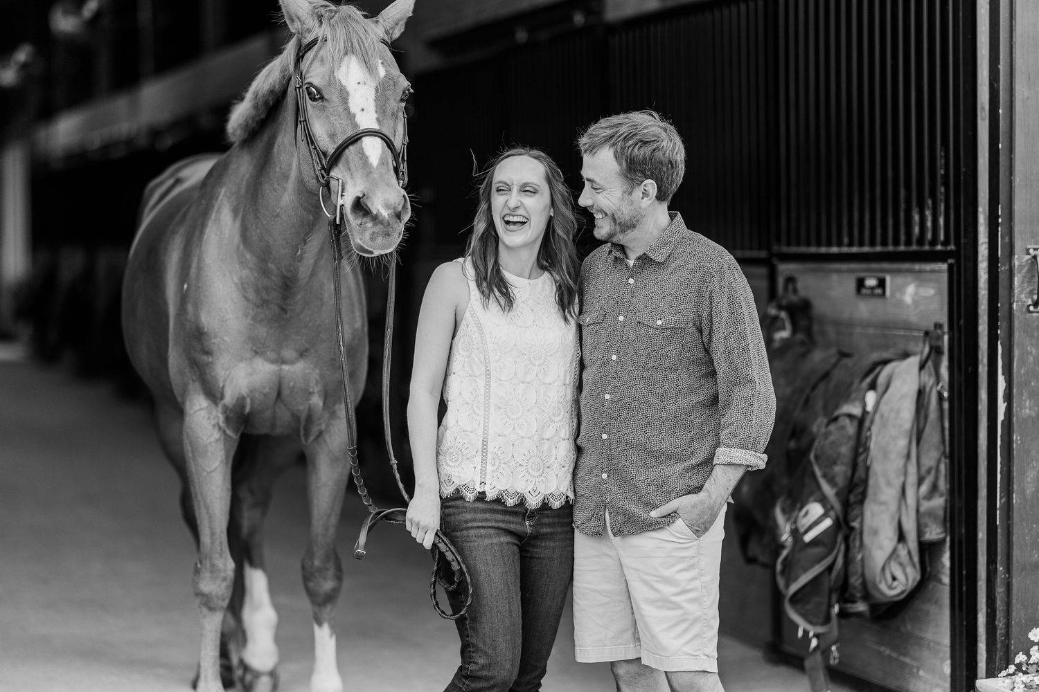 Black and white photo of a couple sharing a moment with their horse in a barn doorway.