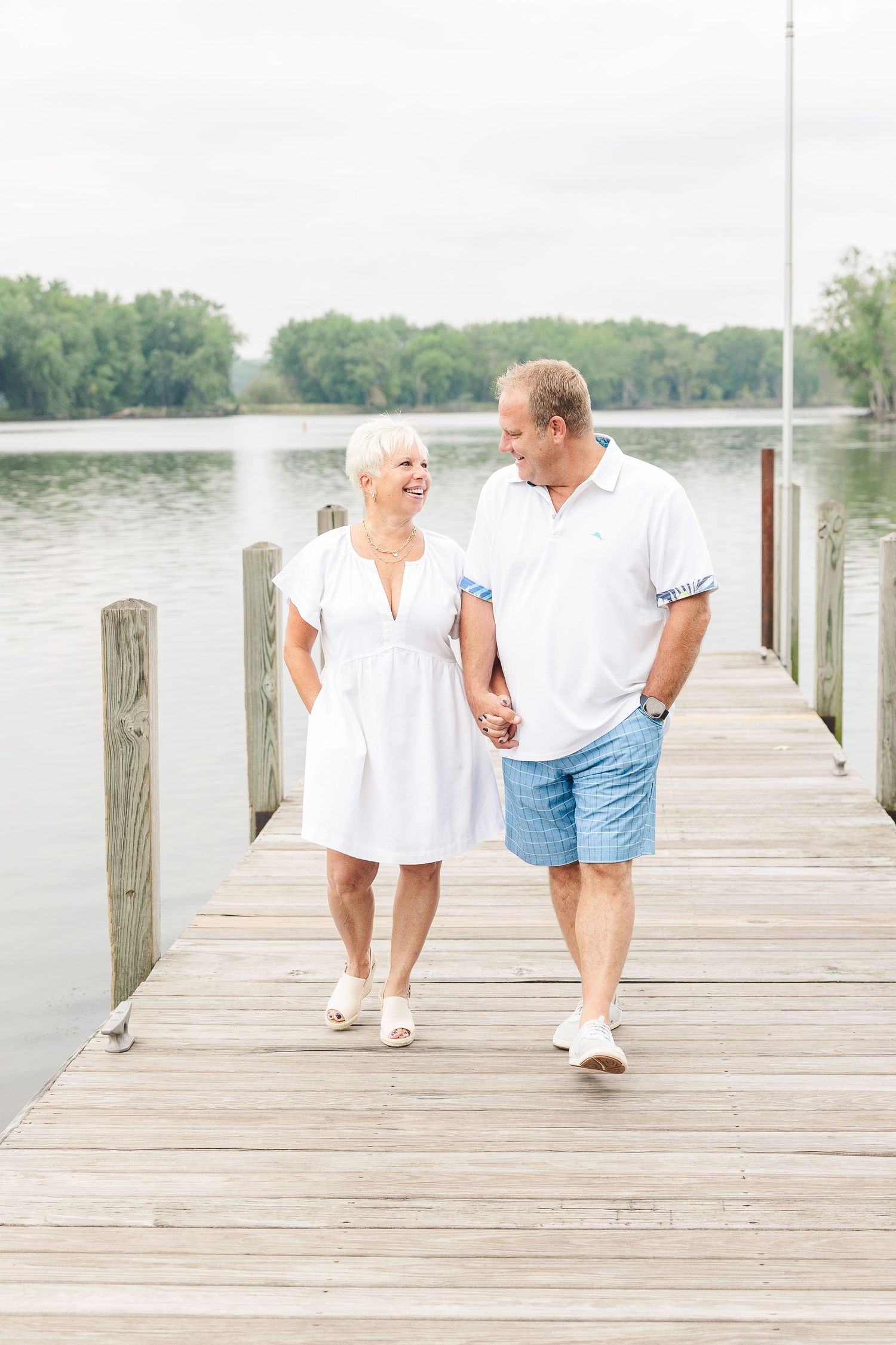 Couple takes romantic stroll along wooden dock with peaceful lake views.